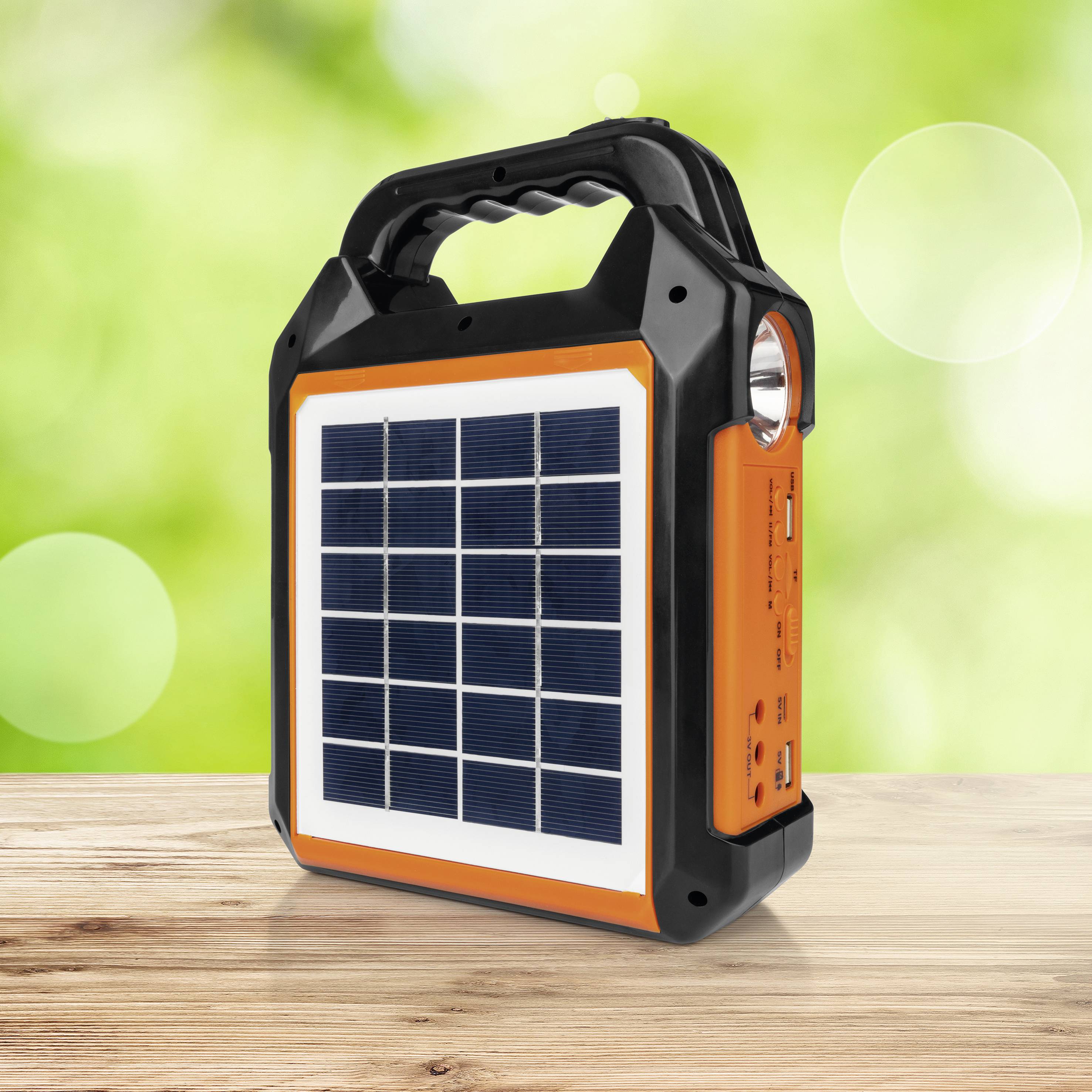 Tragbare orange-schwarze Solarleuchte auf Holztisch, mit Solarzellen auf der Front und seitlichem USB-Anschluss, vor grünem, verschwommenem Hintergrund.
