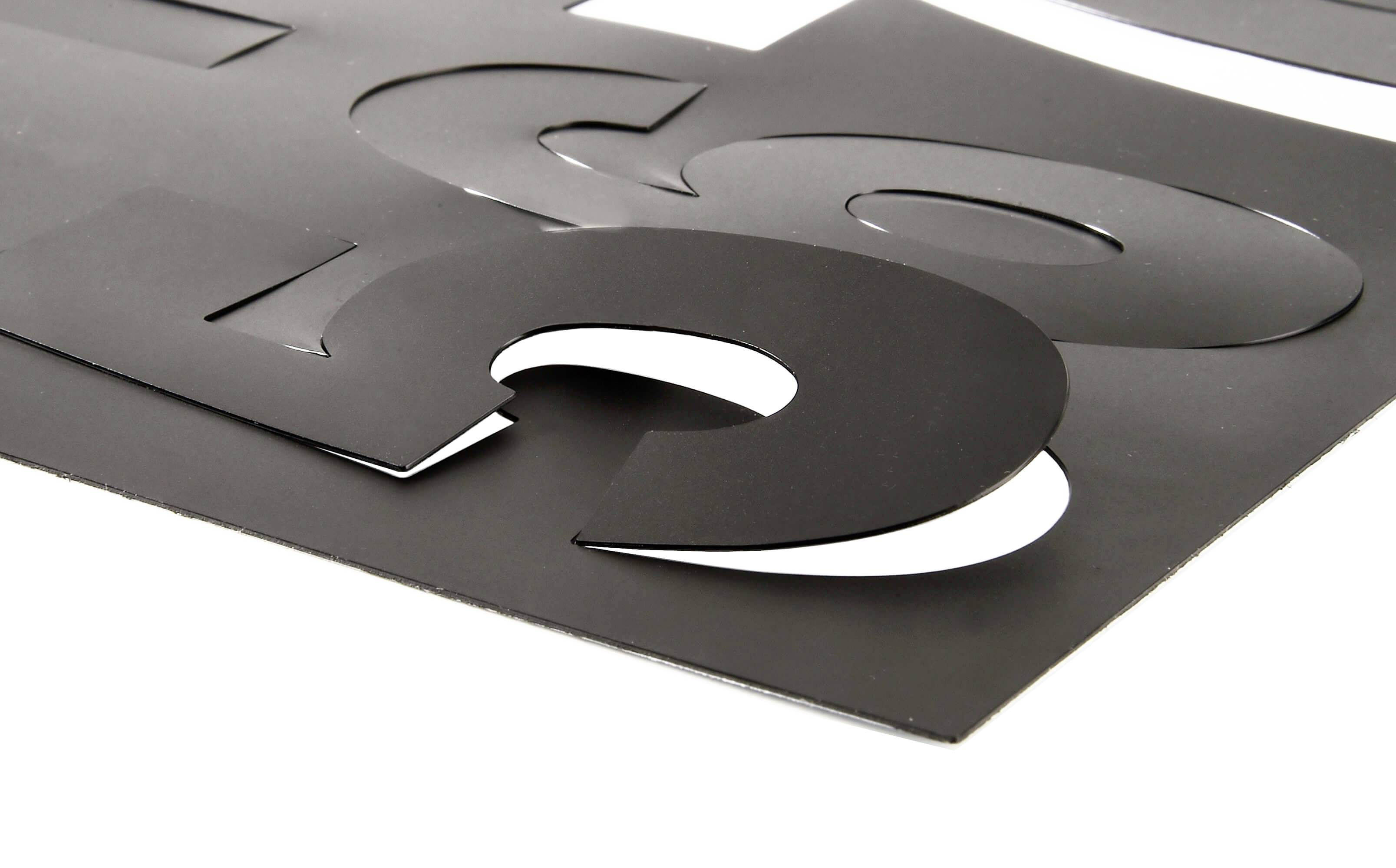 Schwarze, ausgeschnittene Buchstaben auf weißem Hintergrund liegen überlappend auf einer Fläche und erzeugen einen 3D-Effekt.