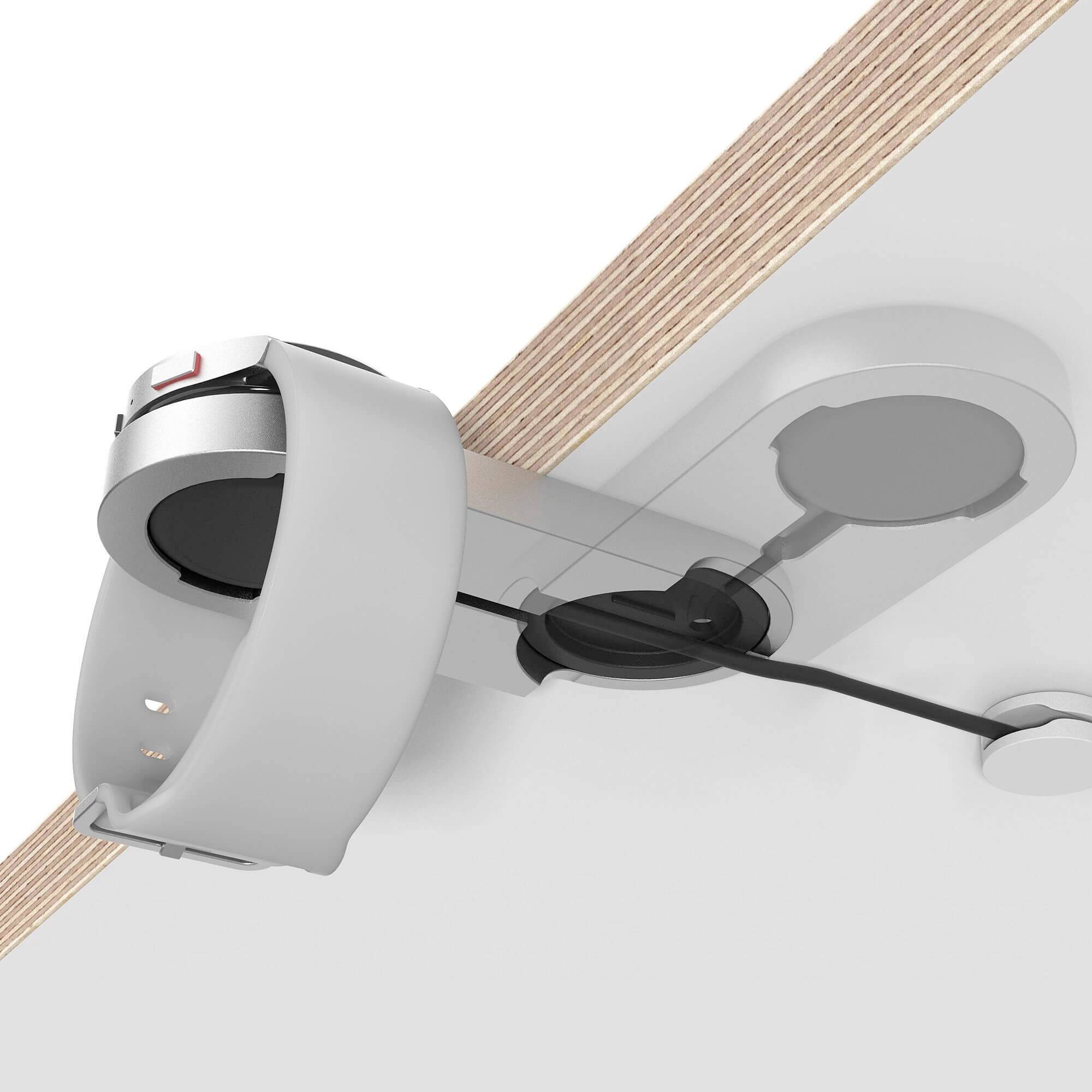 Schwarze Kabelabdeckung und runde Steckdose unter einem Holztisch. Kabel verlaufen von der Steckdose zur Abdeckung, die schließt.