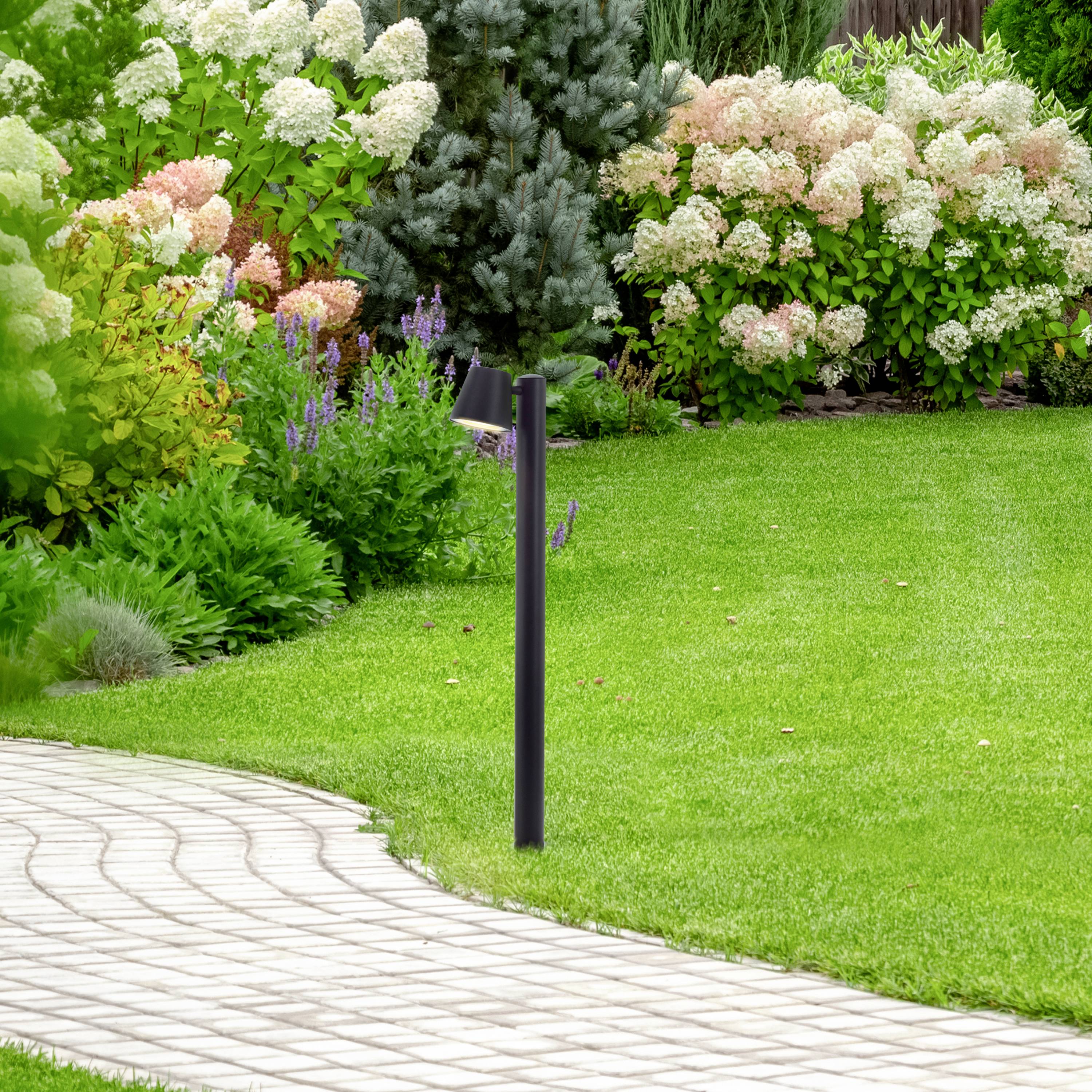 Ein gepflegter Garten mit geschwungenem Pflasterweg, blühenden Hortensien im Hintergrund und einem vereinzelten Nadelbaum im Vordergrund.