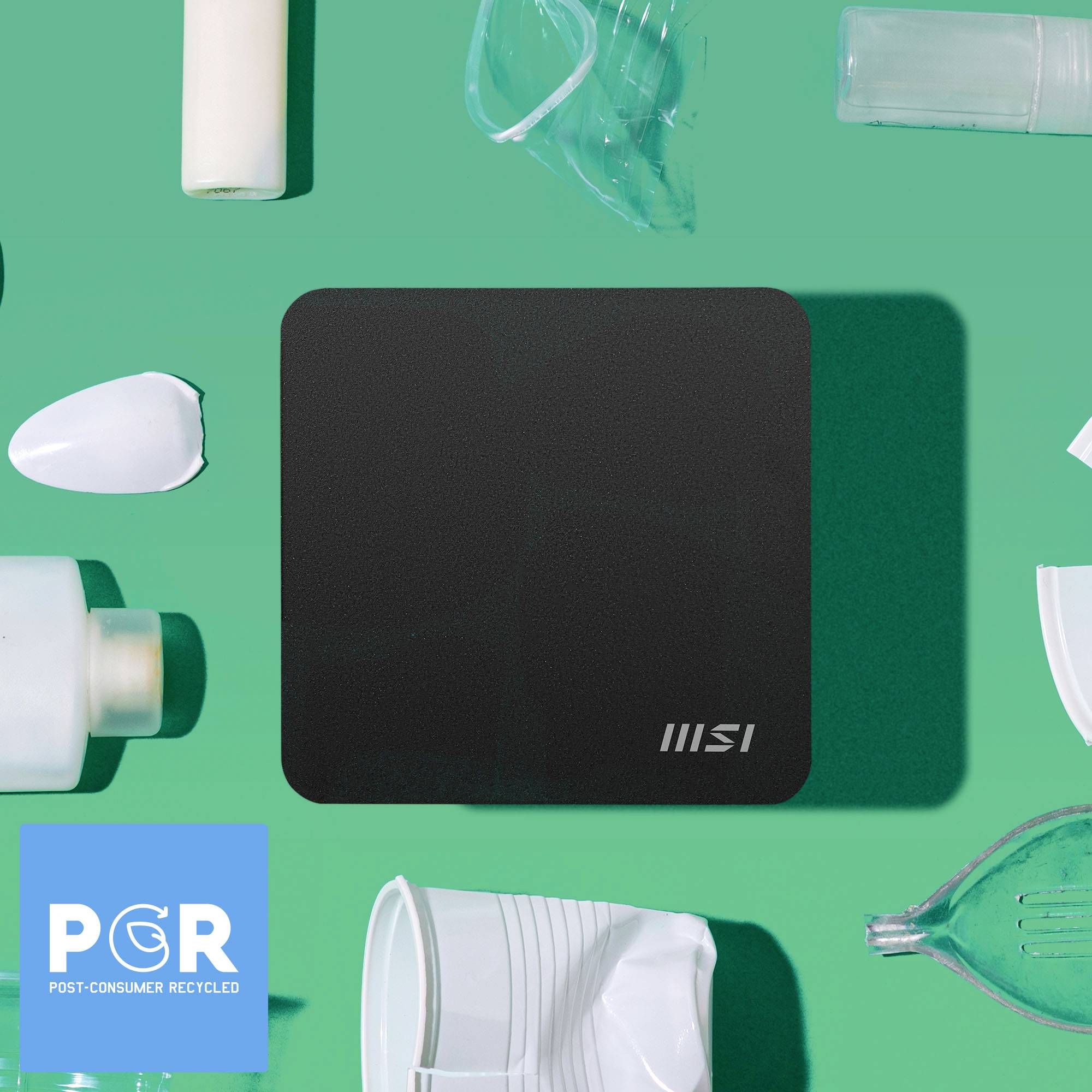 Eine schwarze, rechteckige MSI-Platte umgeben von verschiedenen weißen Plastikgegenständen auf grünem Hintergrund. 'PCR - Post-Consumer Recycled' Logo unten links.