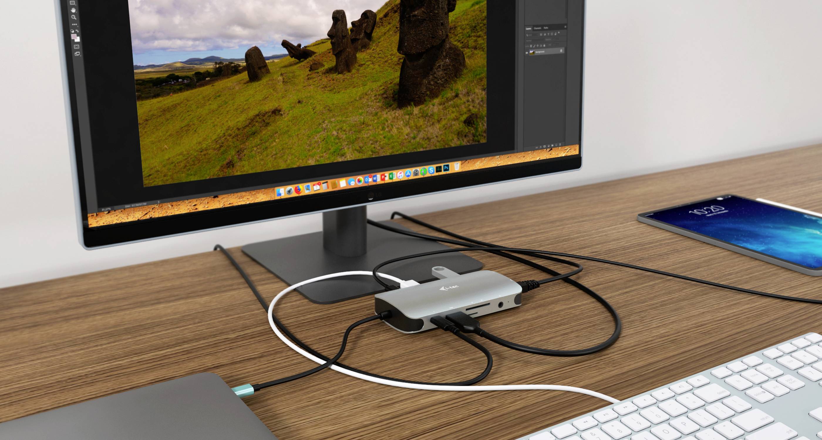 Arbeitsplatz mit Computerbildschirm, der eine Landschaft mit Moai-Statuen zeigt, angeschlossen an mehrere Kabel über einen USB-Hub.
