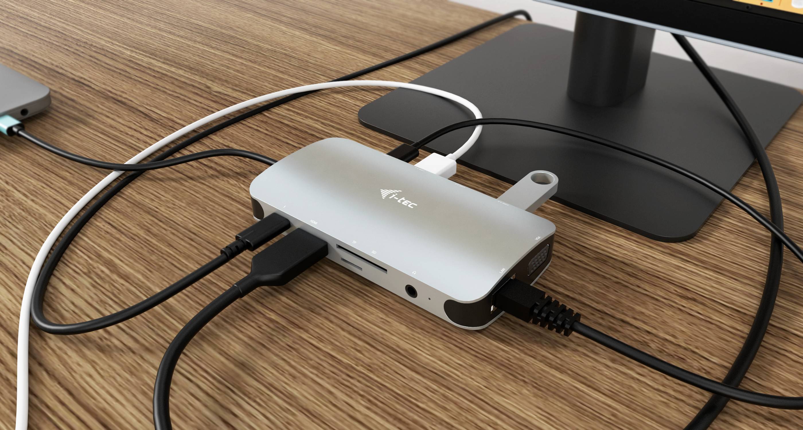Ein USB-C-Hub auf einem Schreibtisch, verbunden mit mehreren Kabeln und Geräten, einschließlich eines Monitors und eines USB-Sticks.