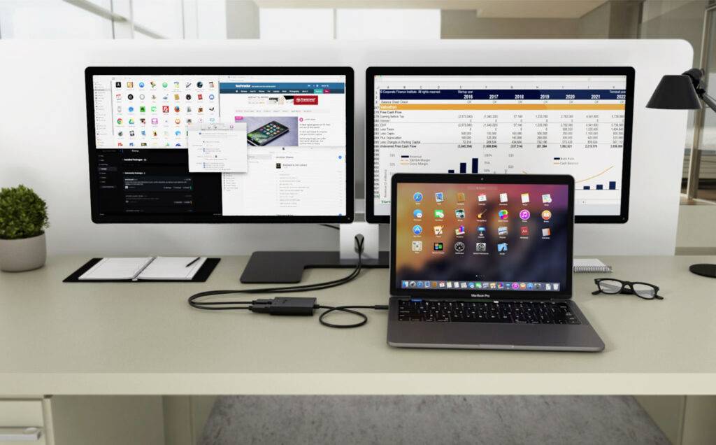 Ein Schreibtisch mit einem Laptop, das an zwei Monitore angeschlossen ist. Die Monitore zeigen eine Website und eine Tabelle an.