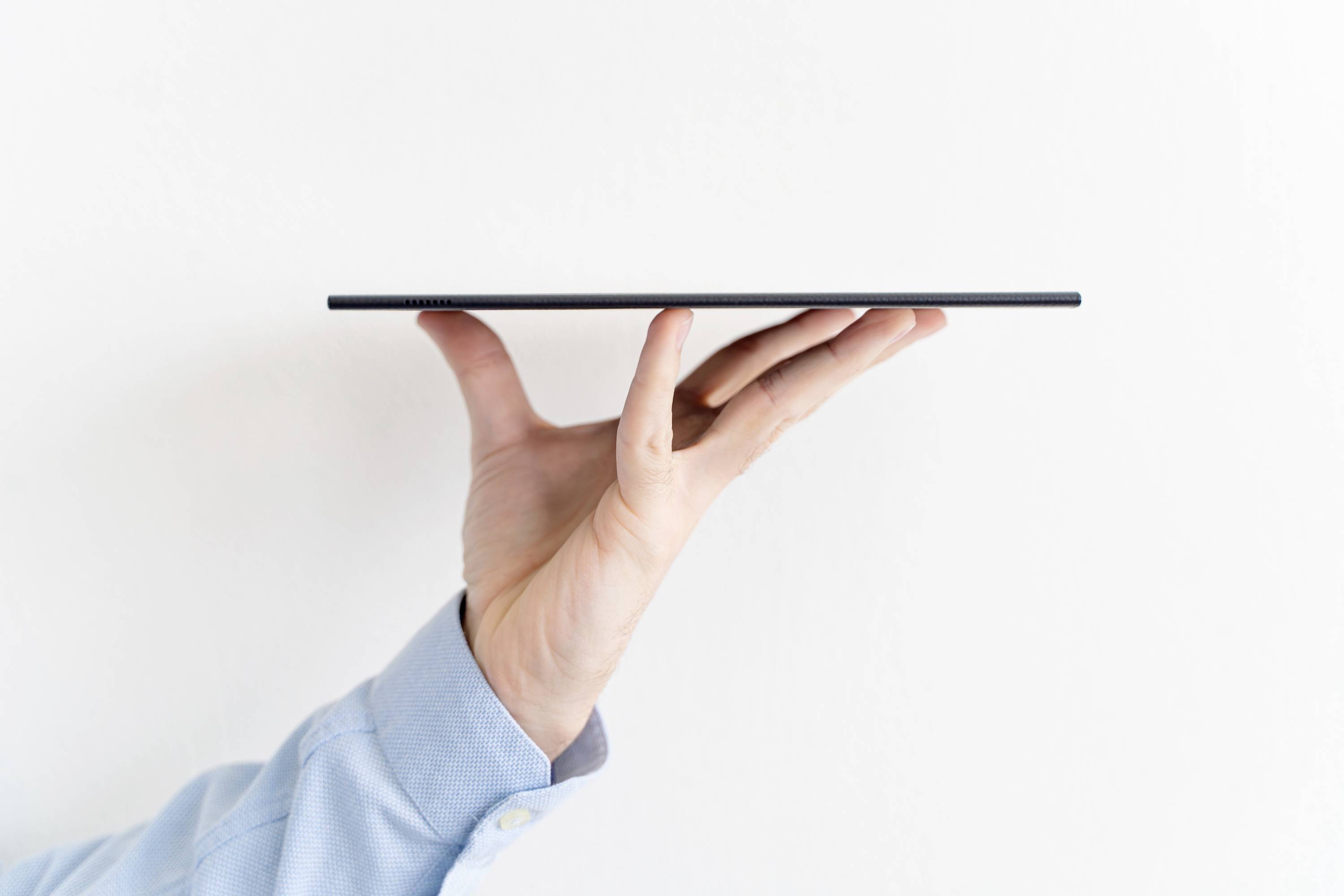Ein Tablet wird von einer Hand balanciert und zeigt seine schlanke Seite. Hintergrund ist weiß.