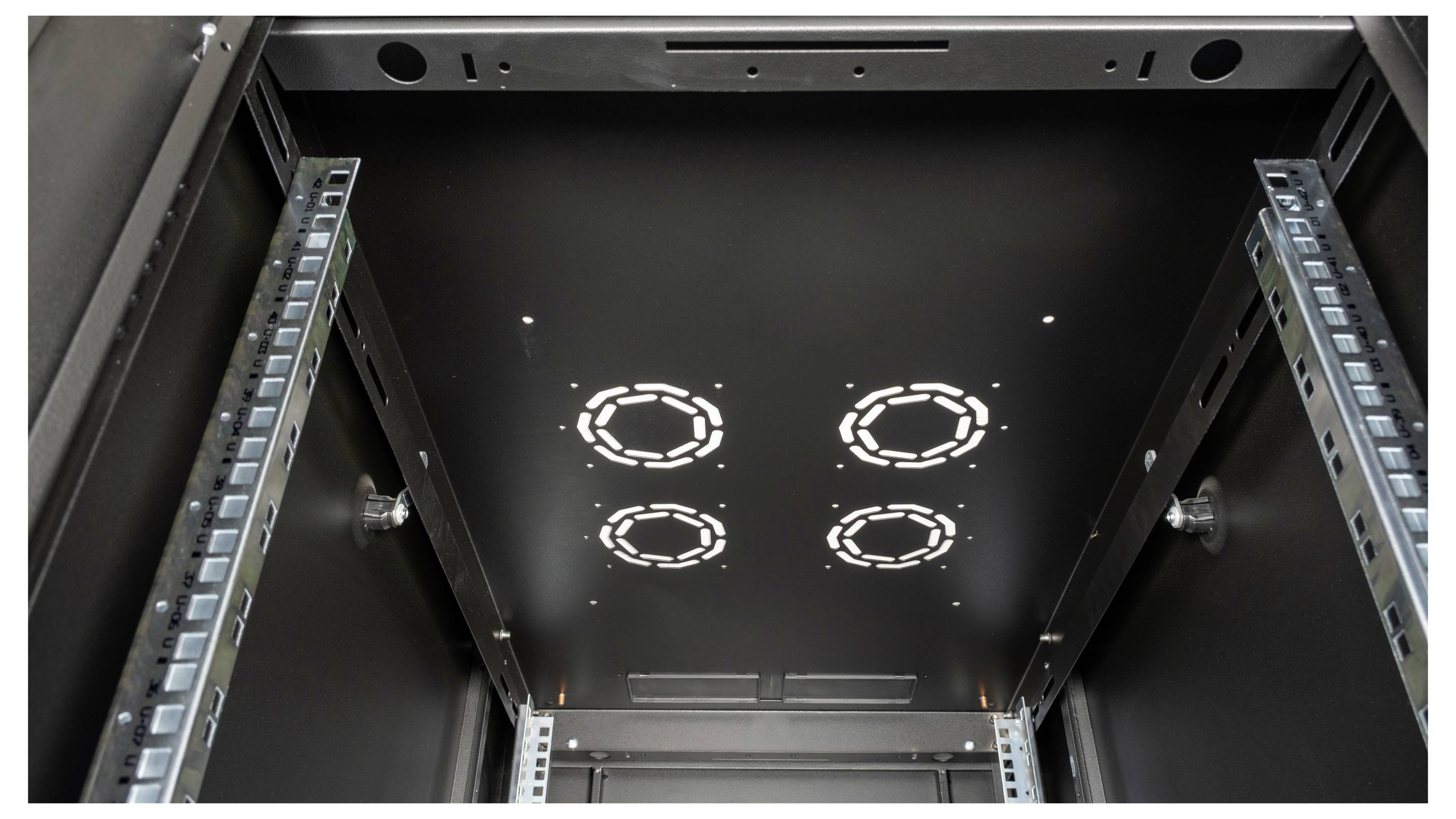 Blick von unten in einen leeren Server-Rack. Metallische Schienen und runde Öffnungen an der Decke für Kabelmanagement sichtbar.