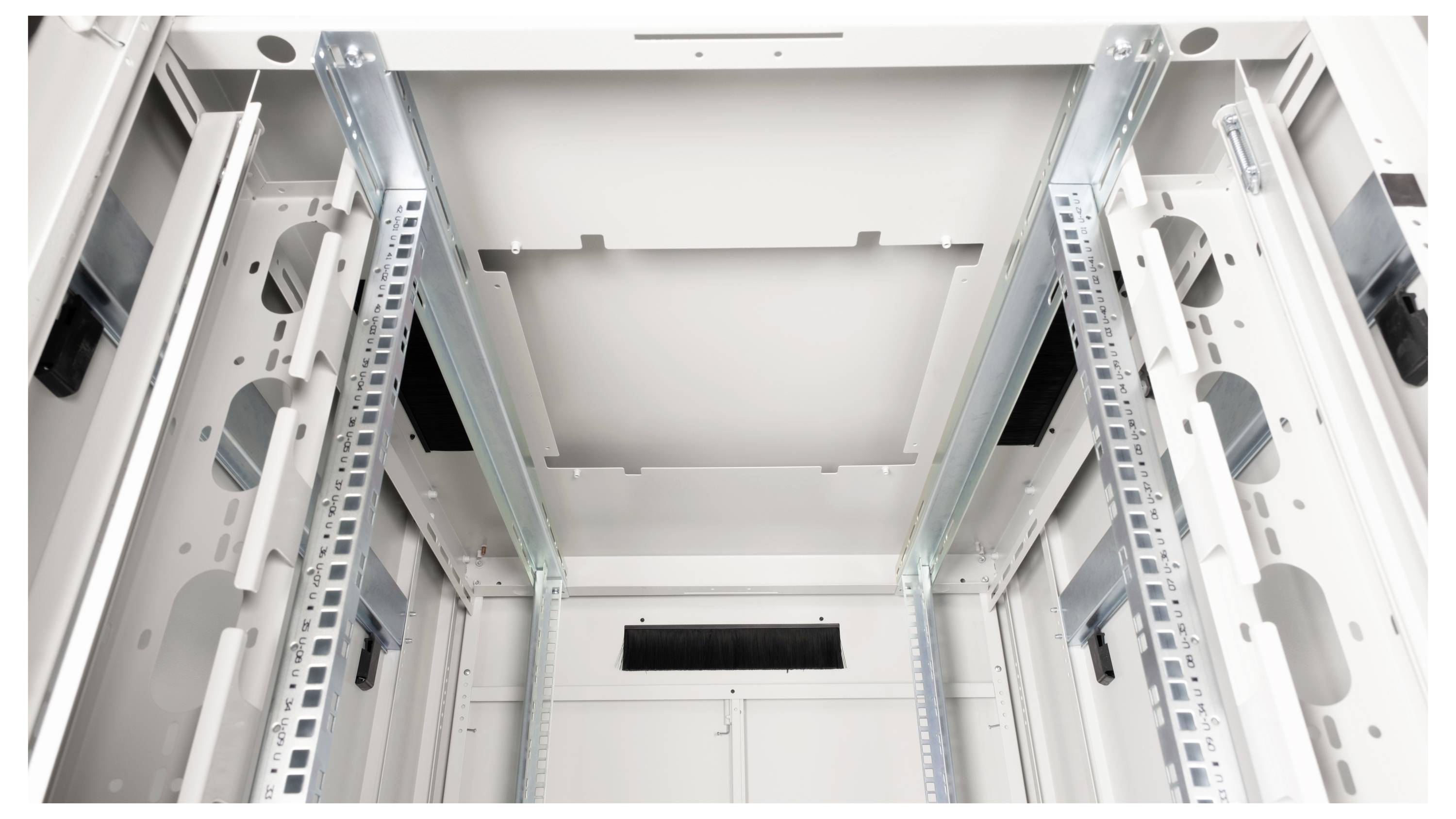 Innenansicht eines leeren, grauen Serverracks mit Metallschienen und Kabeldurchführungen, bereit für die Installation elektronischer Geräte.