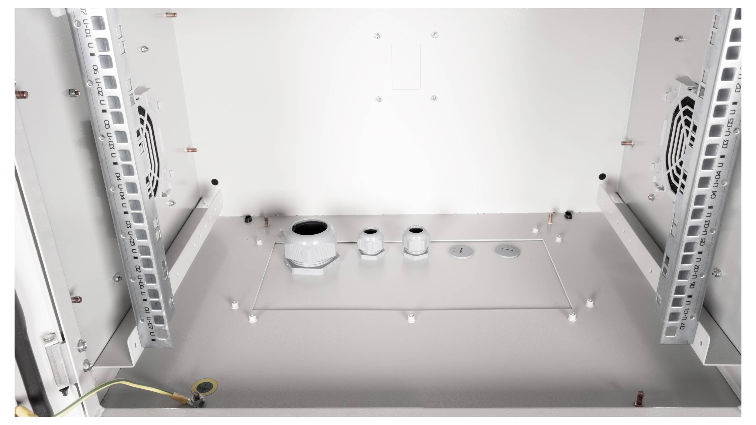 Innenansicht eines leeren Metallgehäuses mit Lüftern an den Seiten und verschiedenen Kabeldurchführungen am Boden.