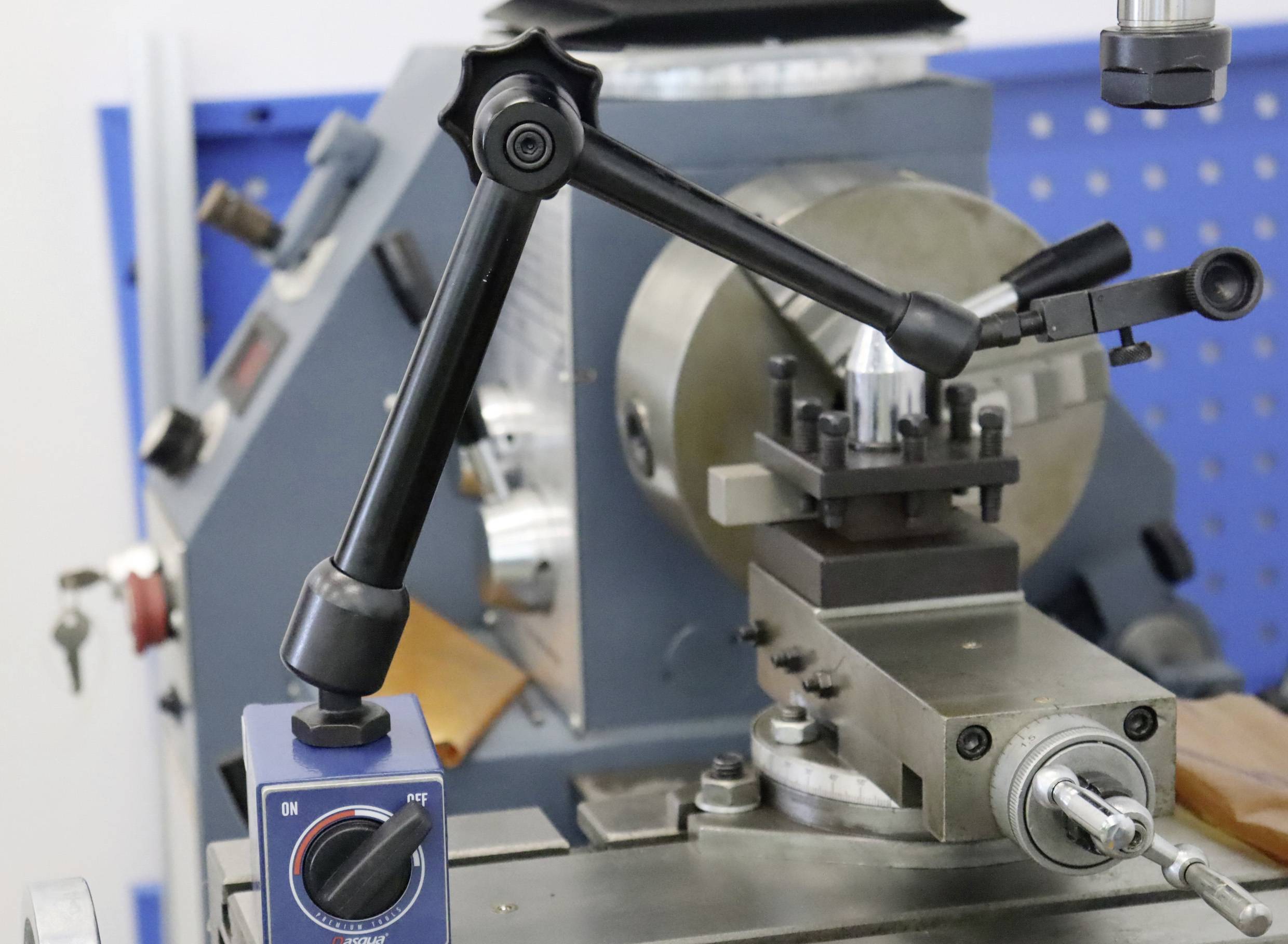 Drehmaschine mit Präzisionseinstellung und Werkzeug, bereit zur Metallbearbeitung. Im Hintergrund blaues Lochblech.