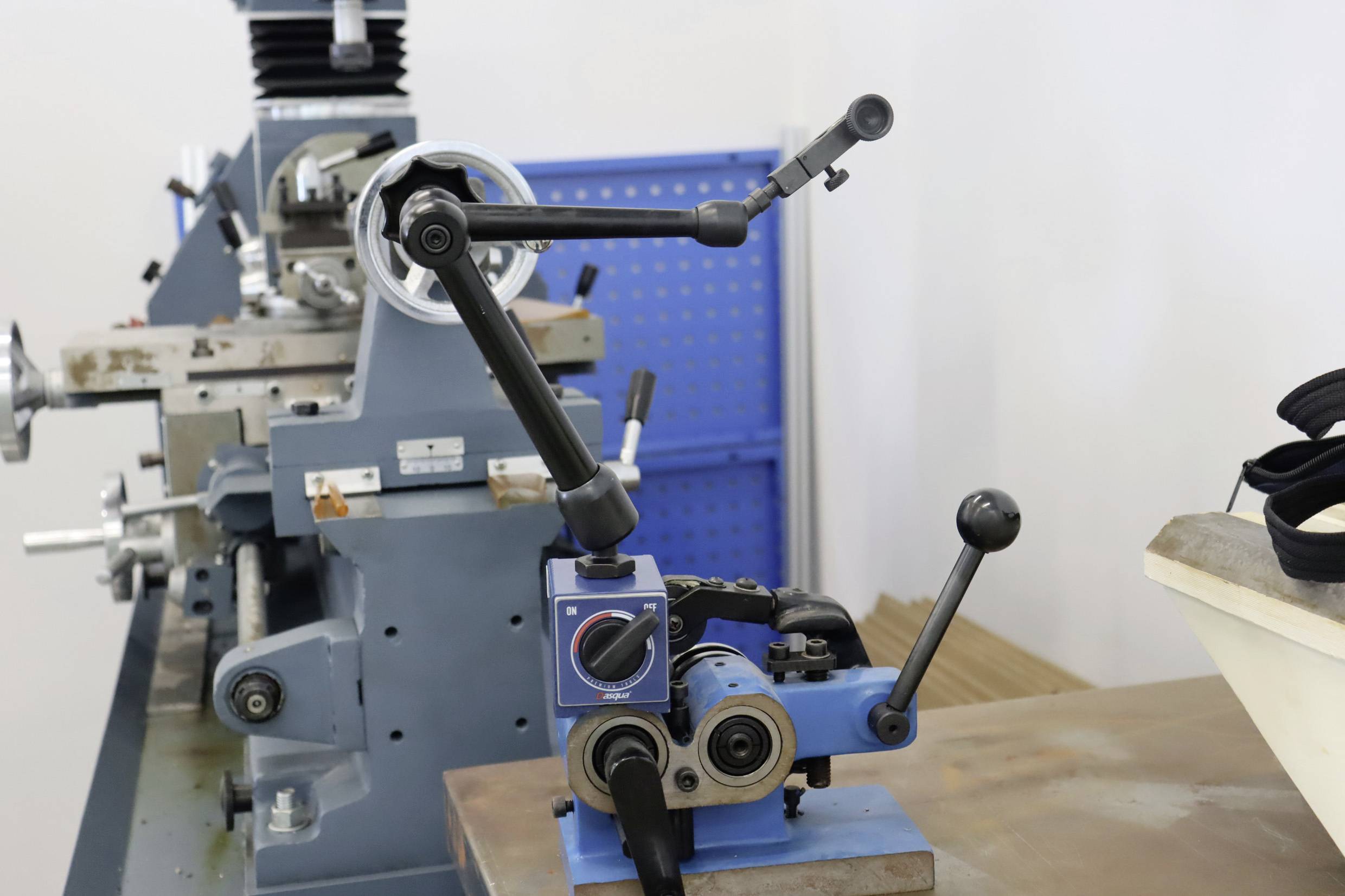 Eine blaue Fräsmaschine mit Hebelarmen und Reglern steht in einem Arbeitsraum. Im Hintergrund ist ein weiteres graues Gerät sichtbar.