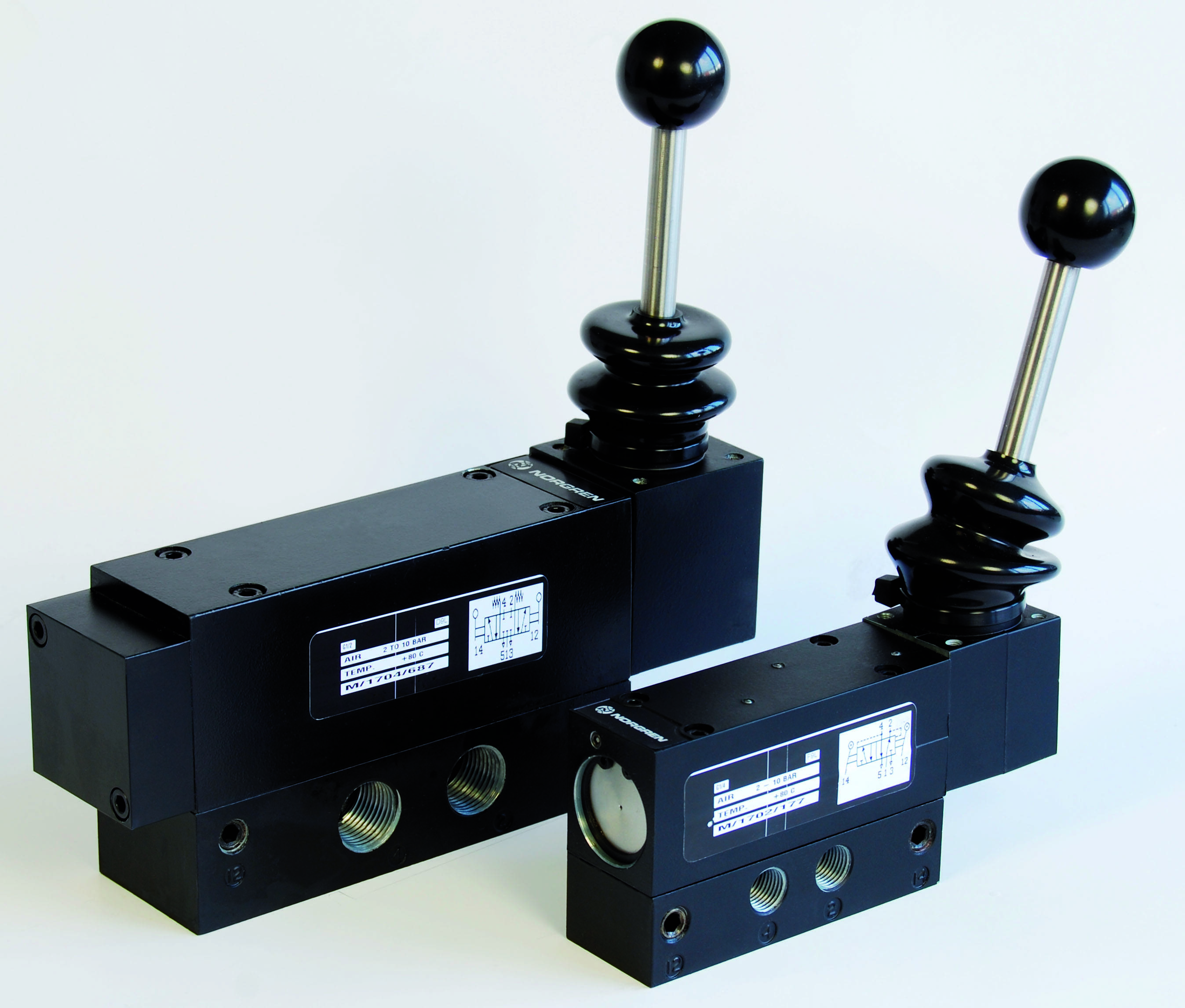 Zwei schwarze hydraulische Umschaltventile mit Hebel, nebeneinander aufgestellt. Ventile haben weiße Etiketten mit technischen Details.