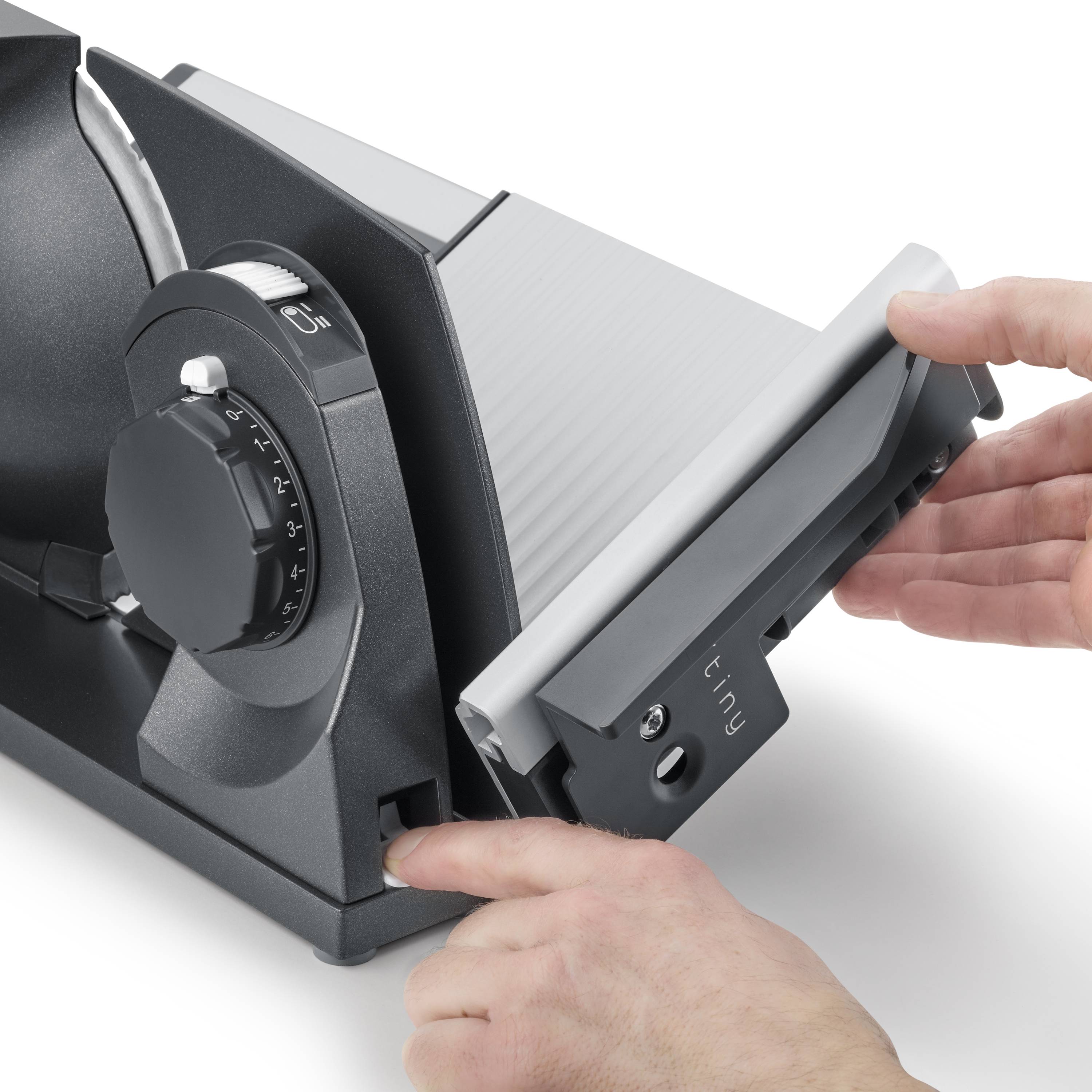 Zwei Hände bedienen eine elektrische Schneidemaschine, die auf dünne Scheiben eingestellt ist.