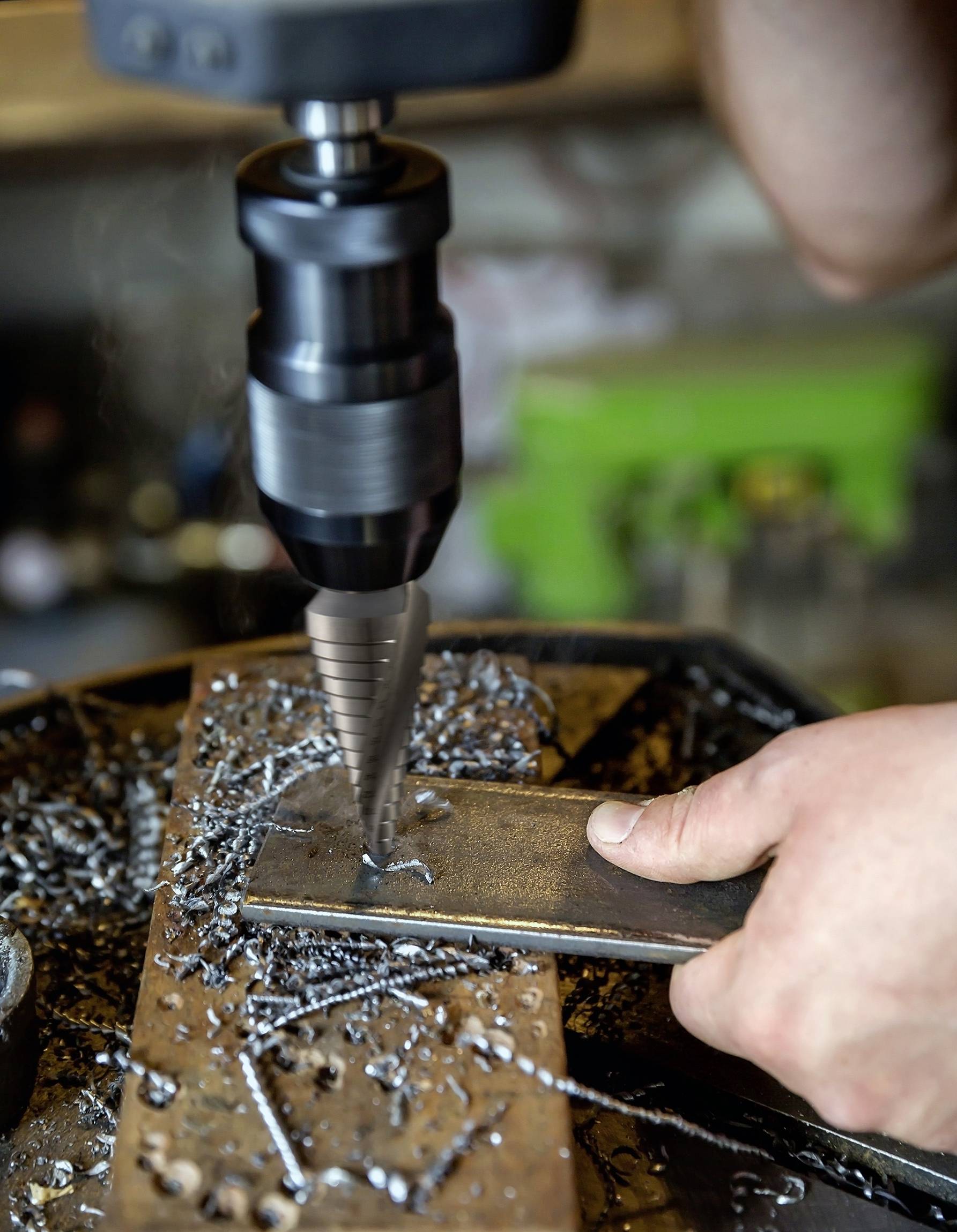 Eine Person verwendet eine Bohrmaschine, um ein Loch in ein Metallstück zu bohren. Metallspäne verteilen sich auf der Arbeitsfläche.