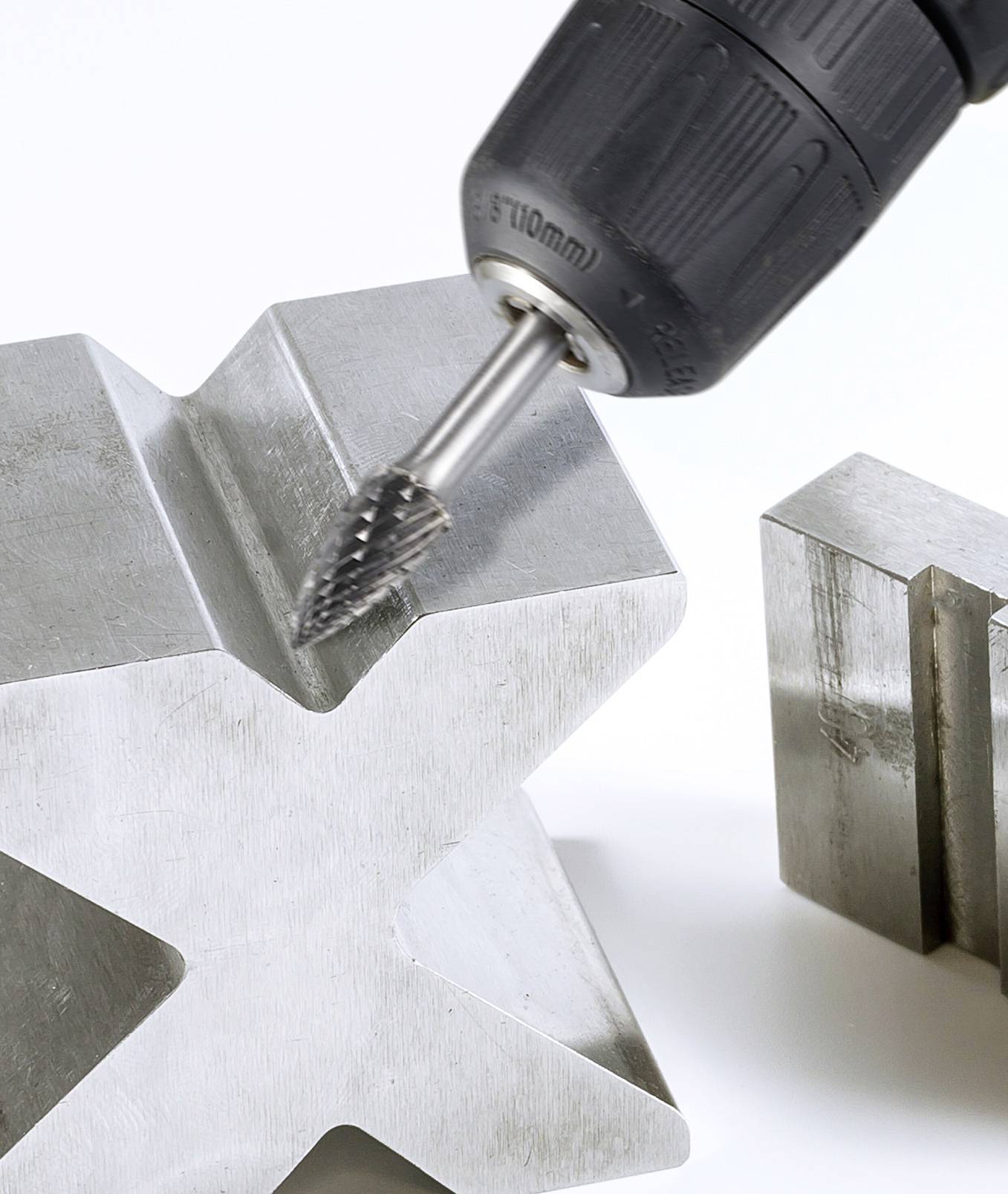 Ein Metallbohrer bearbeitet ein kreuzförmiges Metallstück; zeigt industrielles Werkzeug im Einsatz.