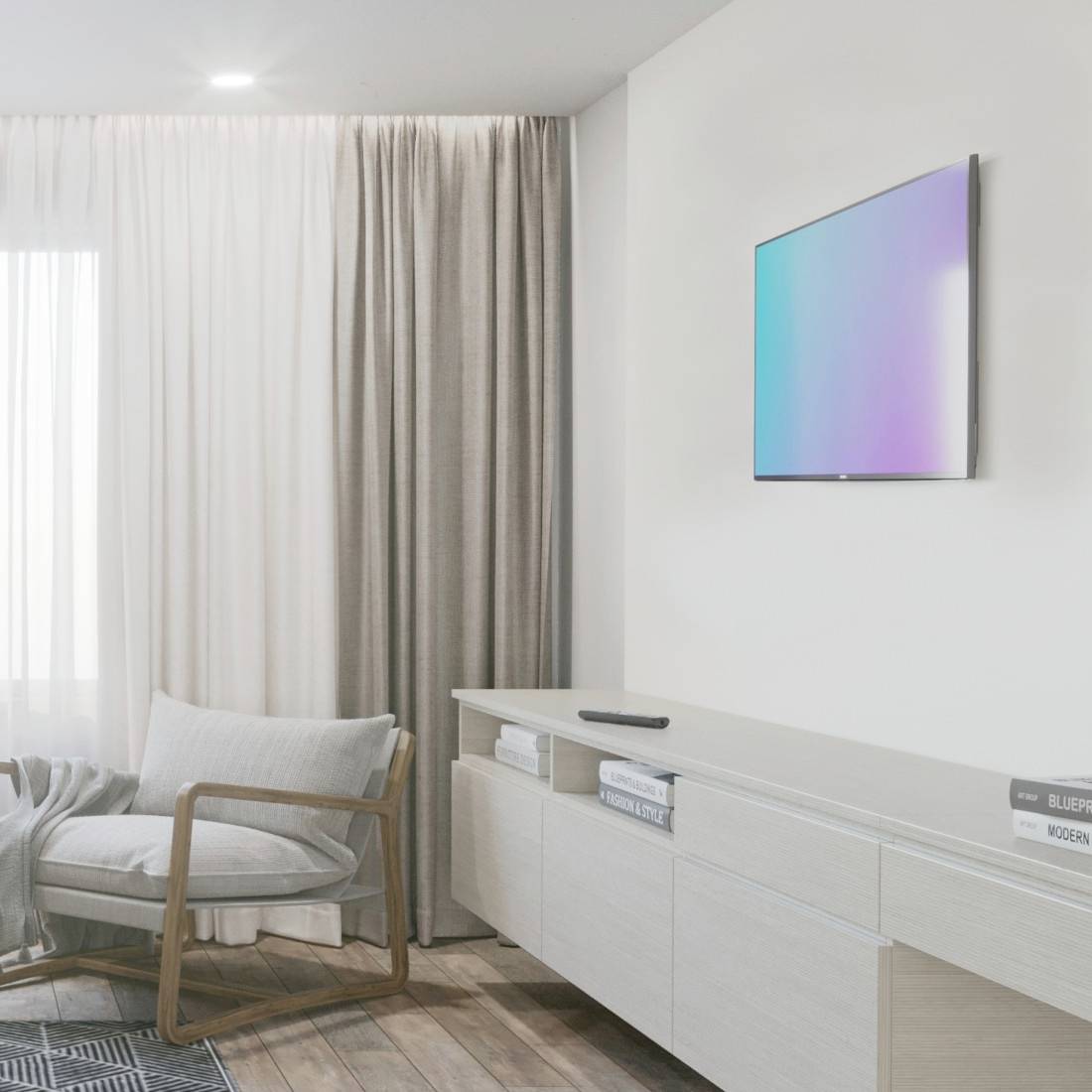 Wohnzimmer mit modernem Stuhl, hellem Vorhang, schlichtem Sideboard, darauf Bücher, und an der Wand ein Flachbildschirm.