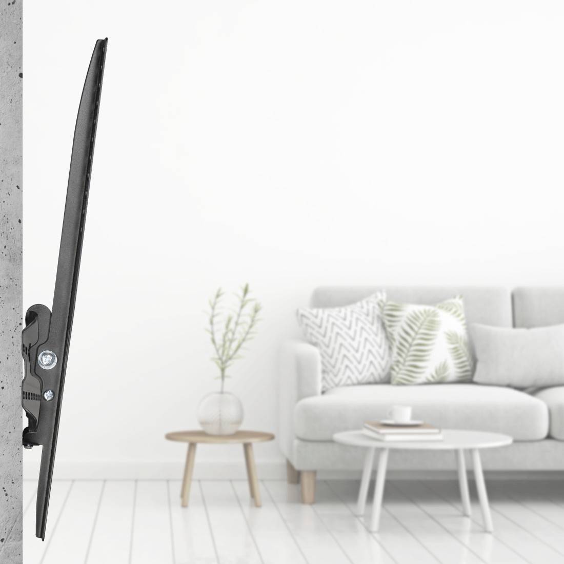 Ein schlanker Fernseher ist an einer grauen Betonwand montiert. Im Hintergrund steht ein Sofa mit Kissen und ein kleiner Tisch mit Pflanzen.