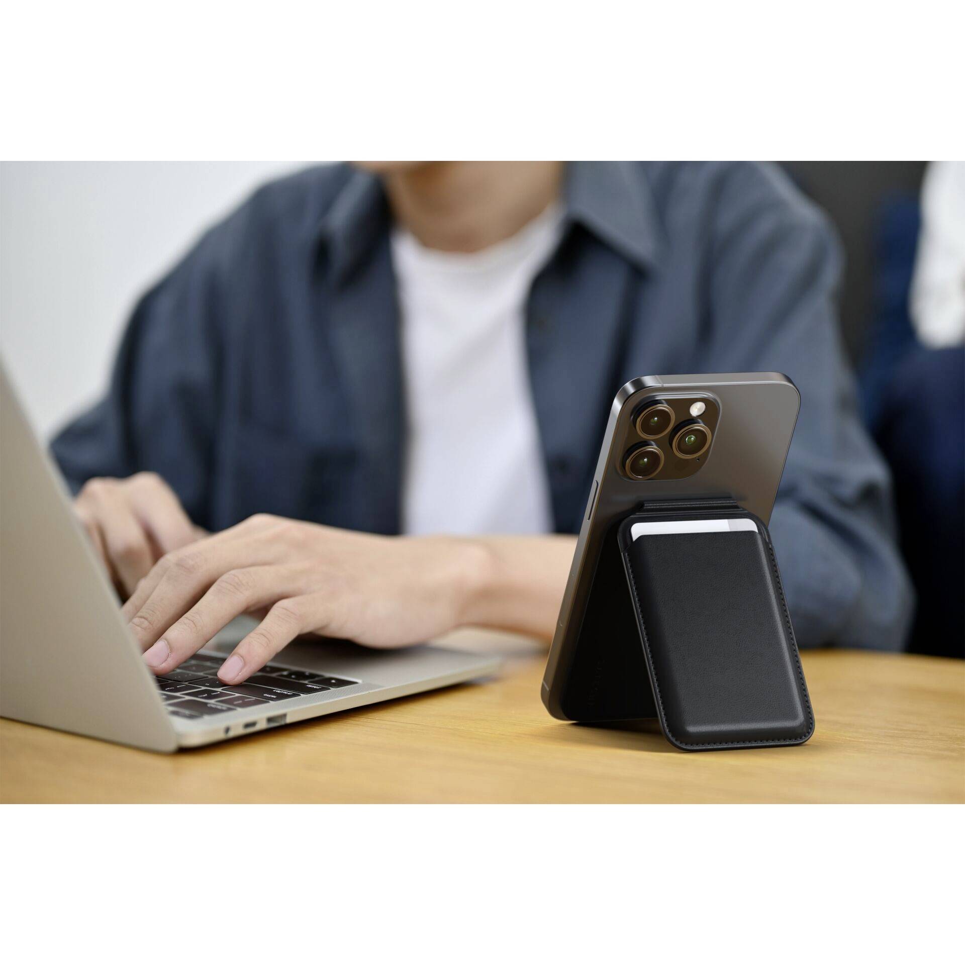 Eine Person tippt auf einem Laptop, während ein Smartphone aufrecht auf einem Tisch steht. Der Fokus liegt auf der mobilen Arbeit.