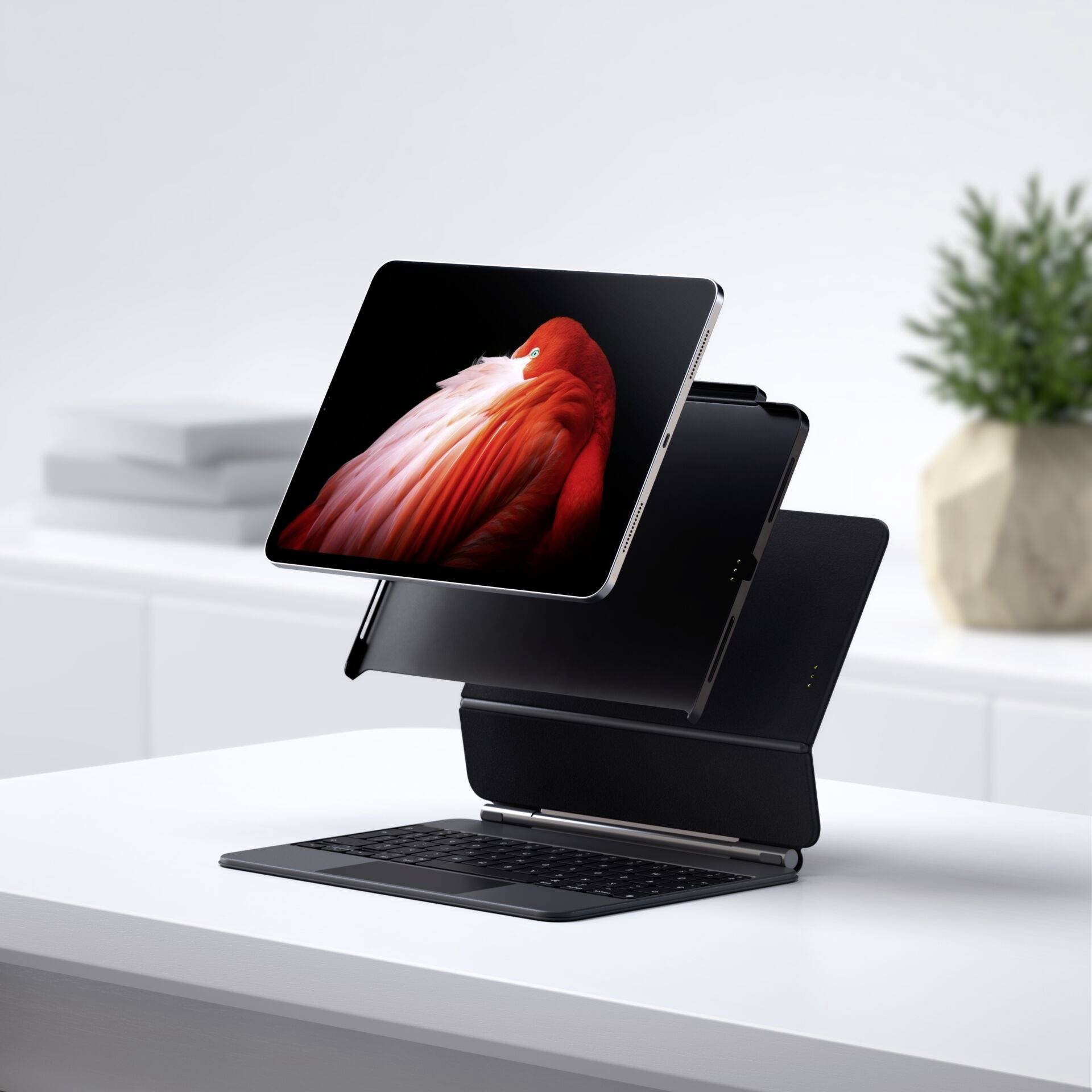 Ein Tablet schwebt über seiner Tastatur auf einem Schreibtisch. Im Hintergrund stehen ein verschlossener Laptop und eine Pflanze.