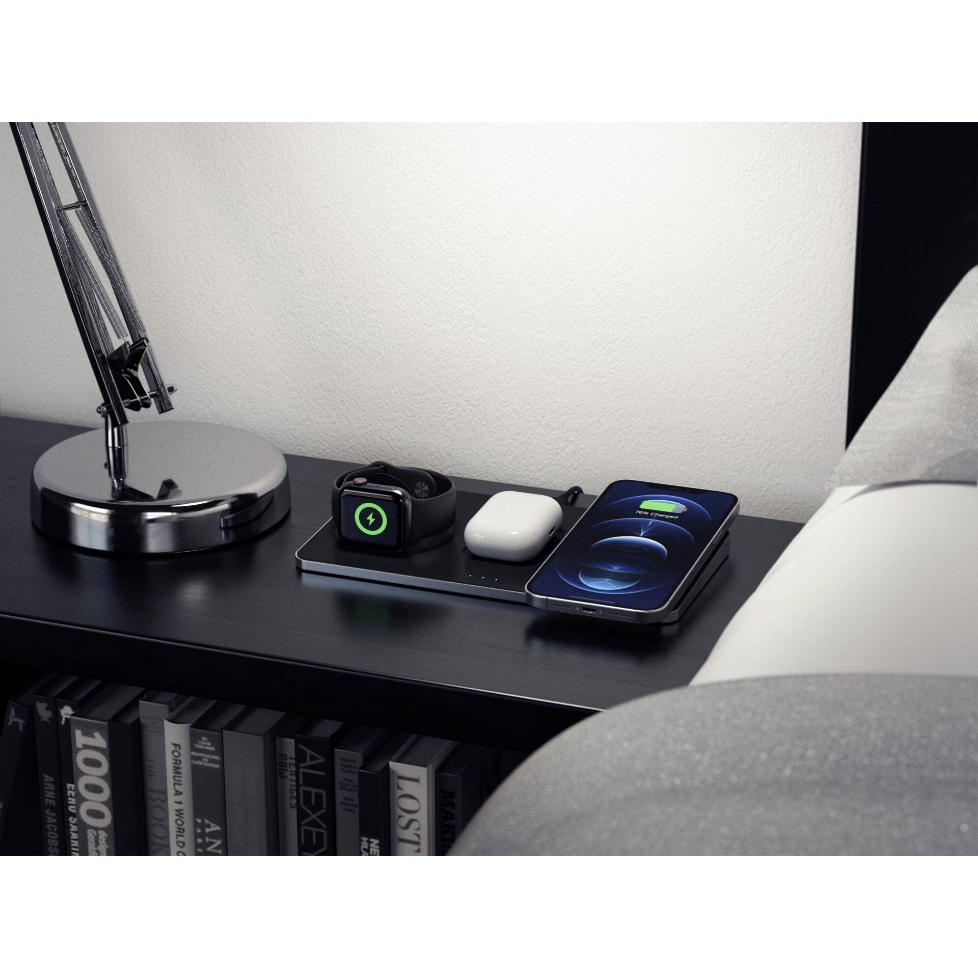 Ein Nachttisch mit einer Lampe, einer Smartwatch, drahtlosen Ohrhörern und einem Smartphone, das auf einer Ladestation liegt.