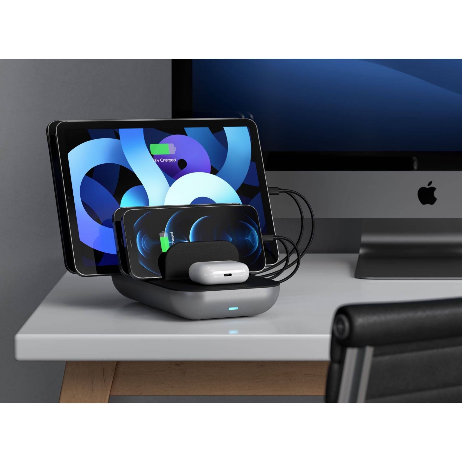 Ein Smartphone, eine Smartwatch und AirPods laden drahtlos auf einer Ladestation neben einem Tablet-Bildschirm und einem Computer.