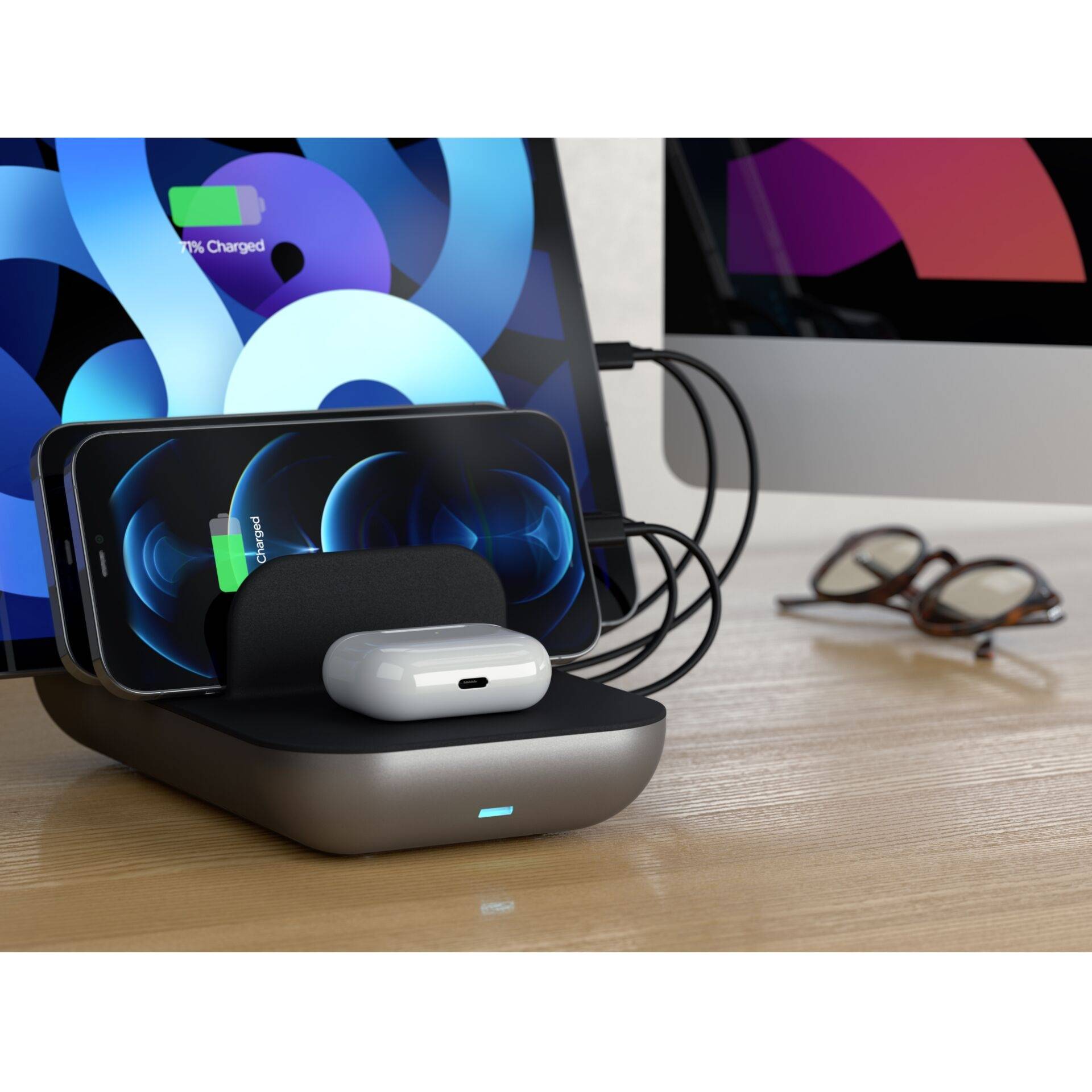 Ein kabelloses Ladegerät lädt ein Smartphone und kabellose Kopfhörer. Im Hintergrund sind ein Monitor und eine Brille zu sehen.