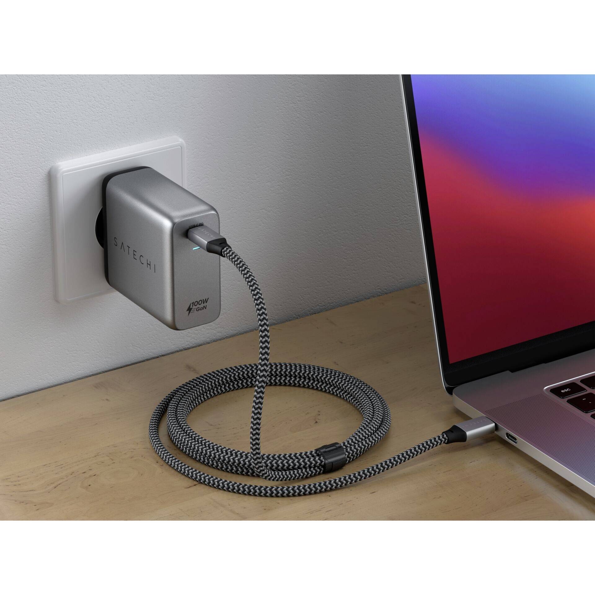 Ein Laptop wird von einem Netzteil an einer Steckdose aufgeladen. Das Netzkabel ist geflochten und mit einem Laptop verbunden, der einen Bildschirm zeigt.