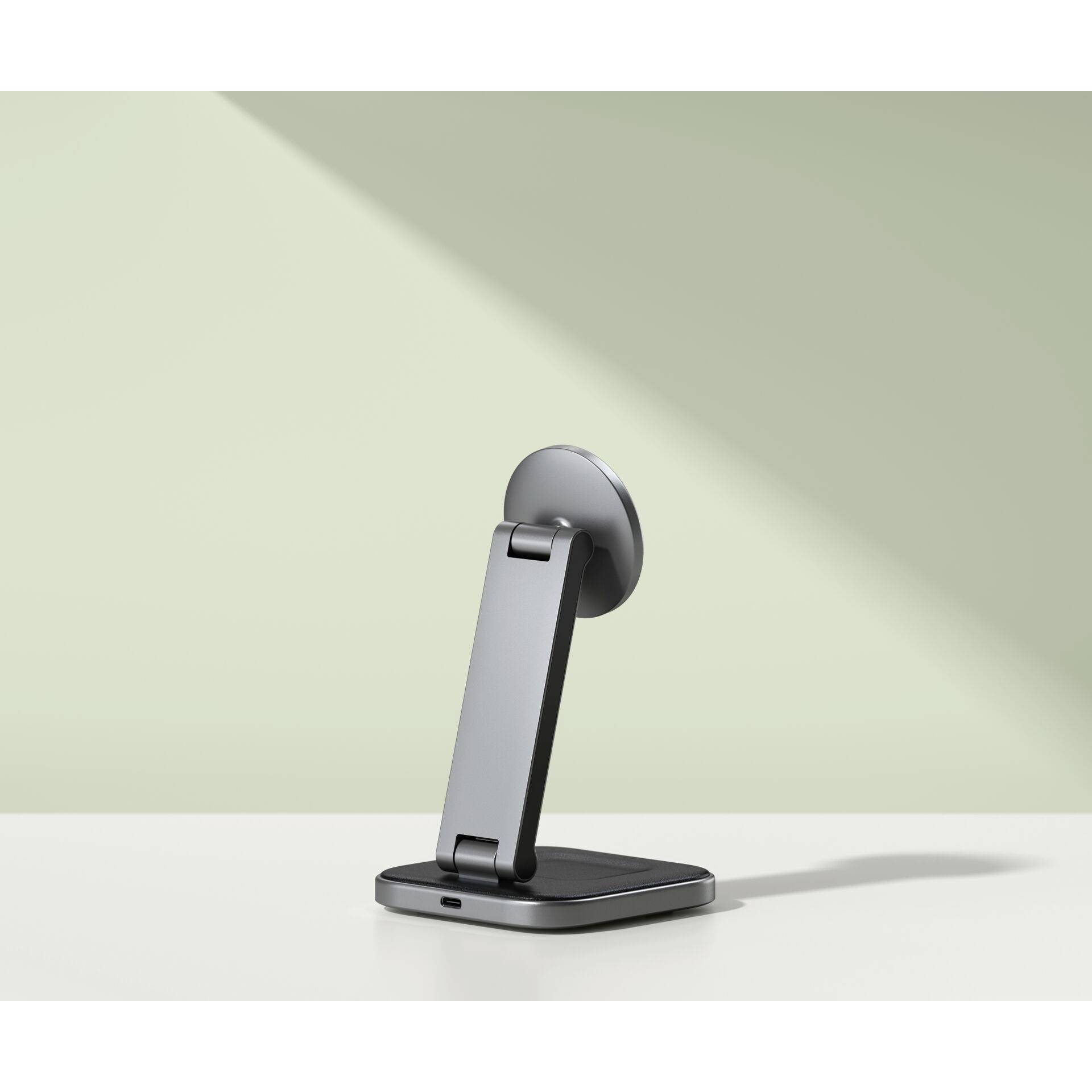 Ein grauer Handyhalter steht aufrecht auf einer weißen Fläche vor einer hellgrünen Wand im Hintergrund.