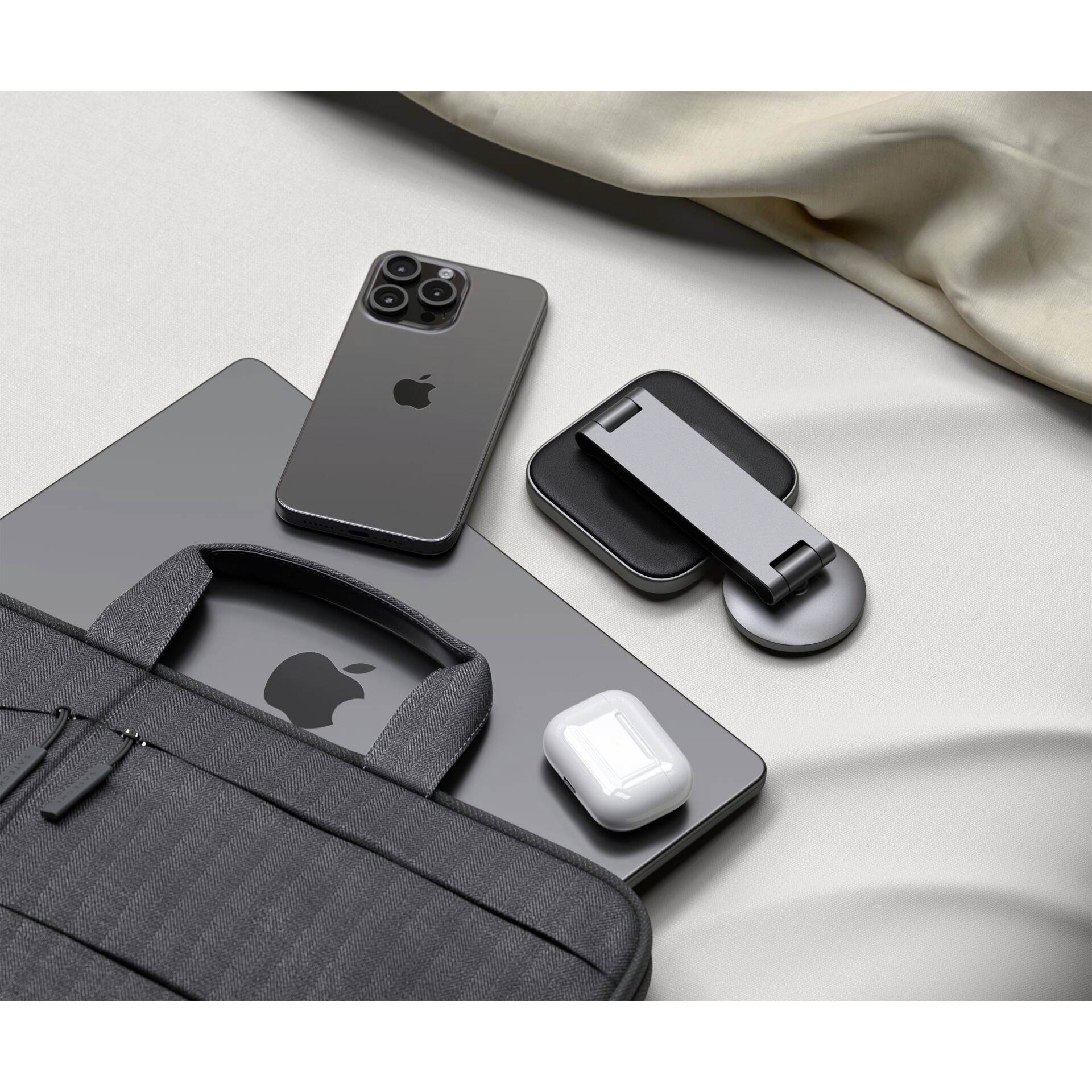 Laptop, Smartphone, AirPods und Zubehör auf einem Bett neben einer schwarzen Tasche. Tech-Produkte werden ordentlich arrangiert gezeigt.