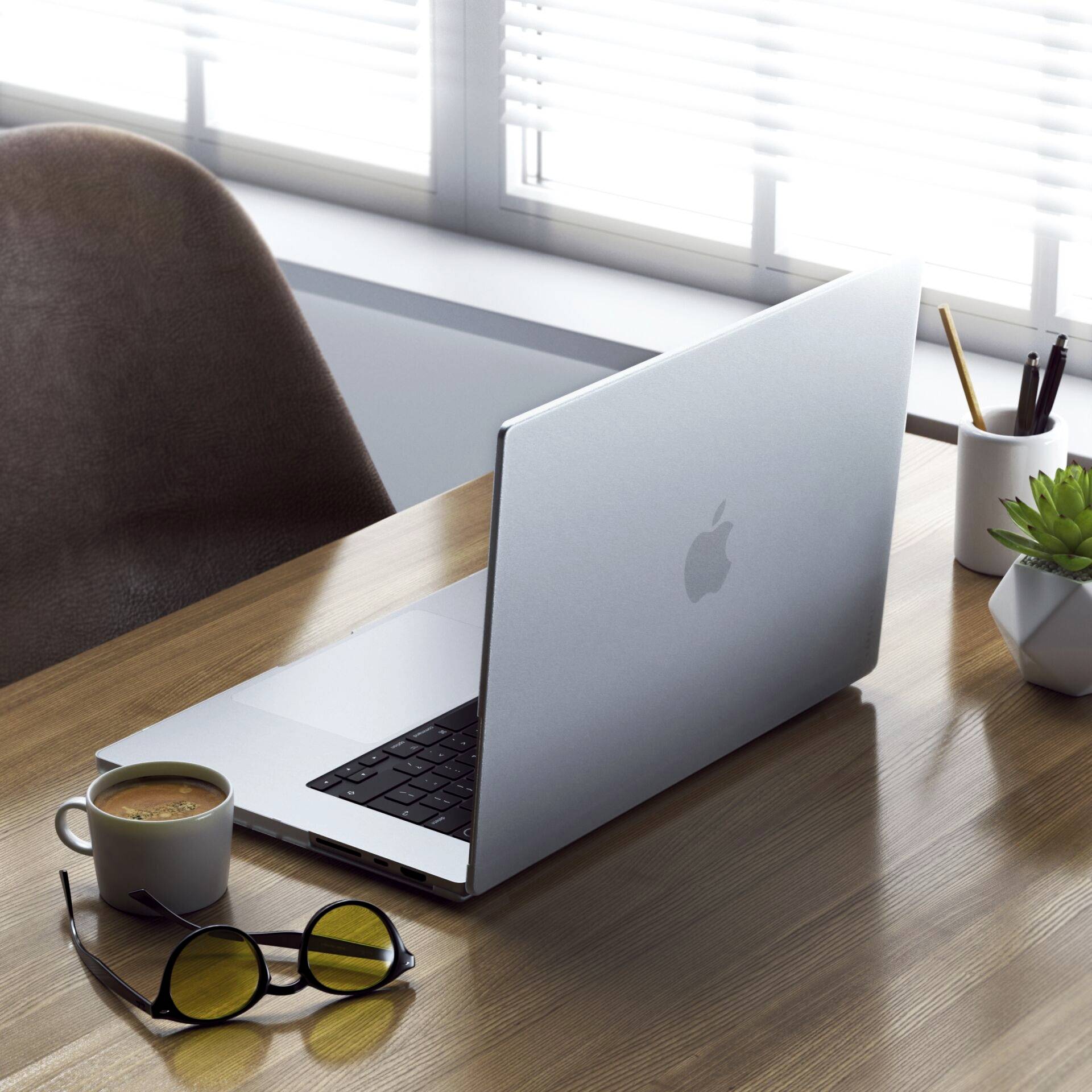 Ein Laptop steht auf einem Schreibtisch neben einer Brille und einem Pflanzentopf. Im Hintergrund ist ein Fenster mit Jalousie zu sehen.