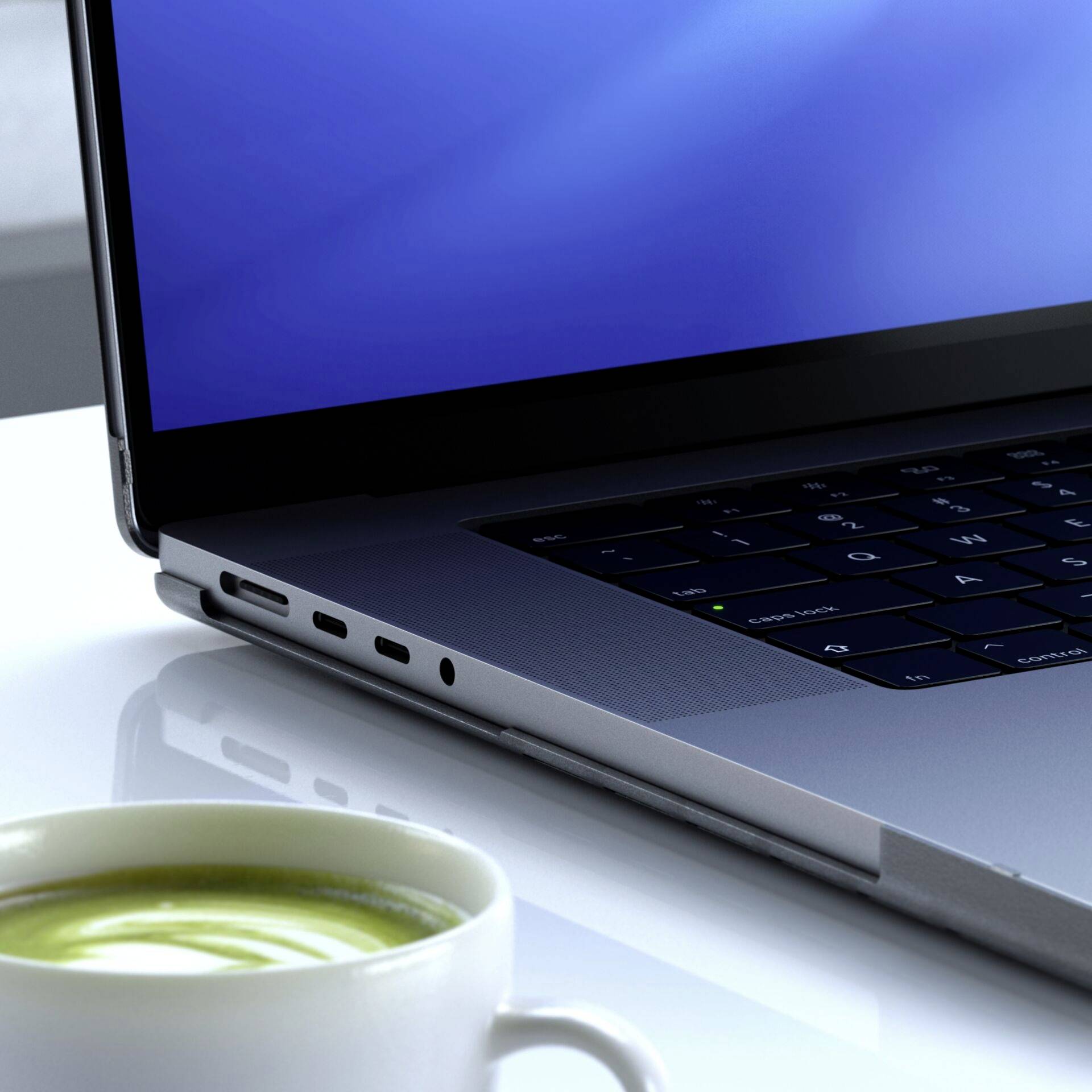 Ein Laptop auf einem Tisch mit einer Tasse grünem Tee im Vordergrund. Der Bildschirm zeigt einen blauen Hintergrund ohne Text.