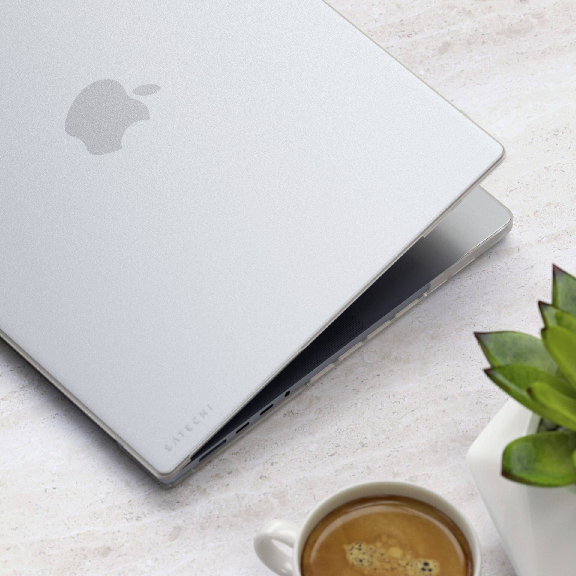 Ein silbernes Laptop liegt halb geöffnet auf einem Schreibtisch neben einer Tasse Kaffee und einer kleinen Pflanze.