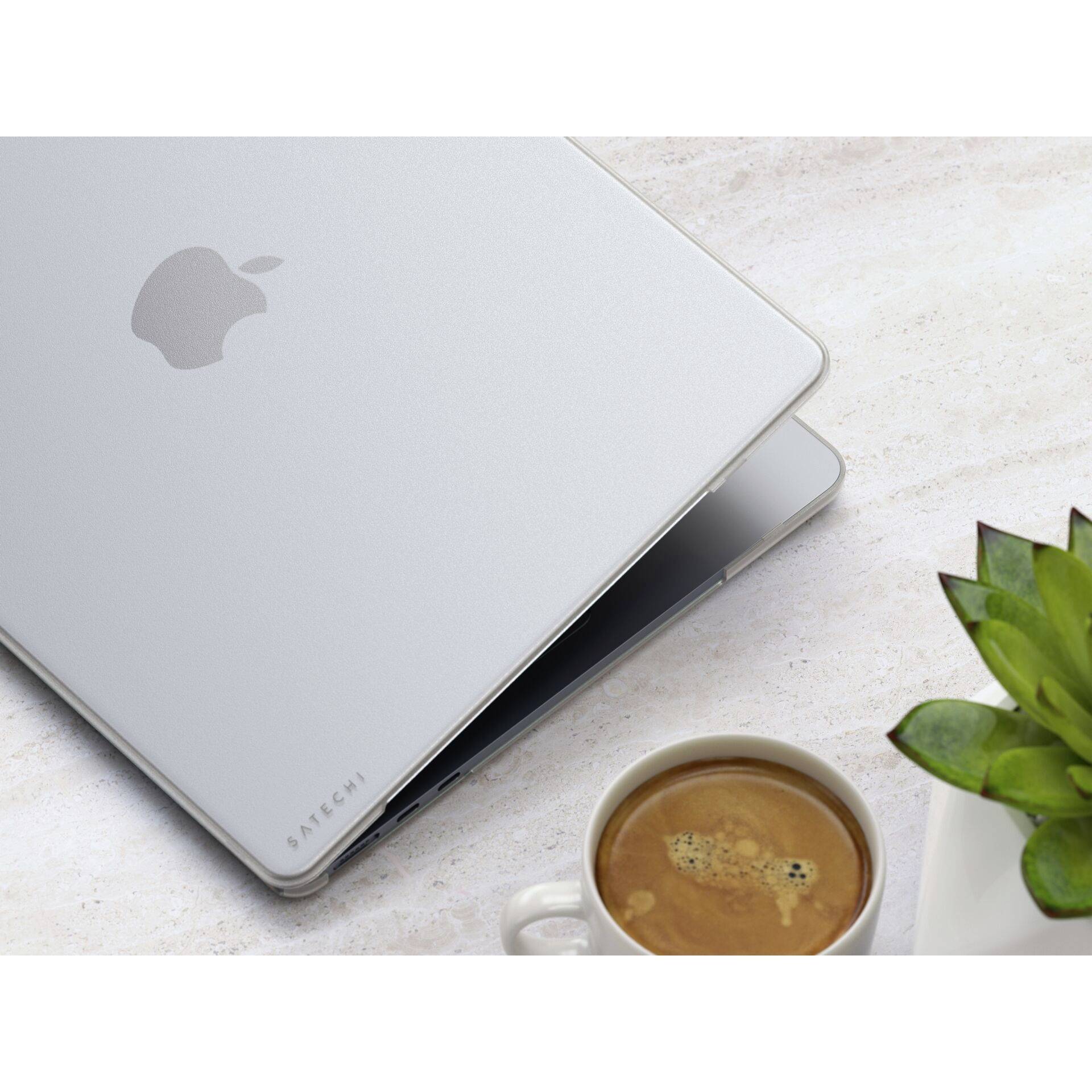 Laptop in silberner Hülle teilweise geöffnet, daneben eine Tasse Kaffee und eine Pflanze auf einem hellen Tisch.