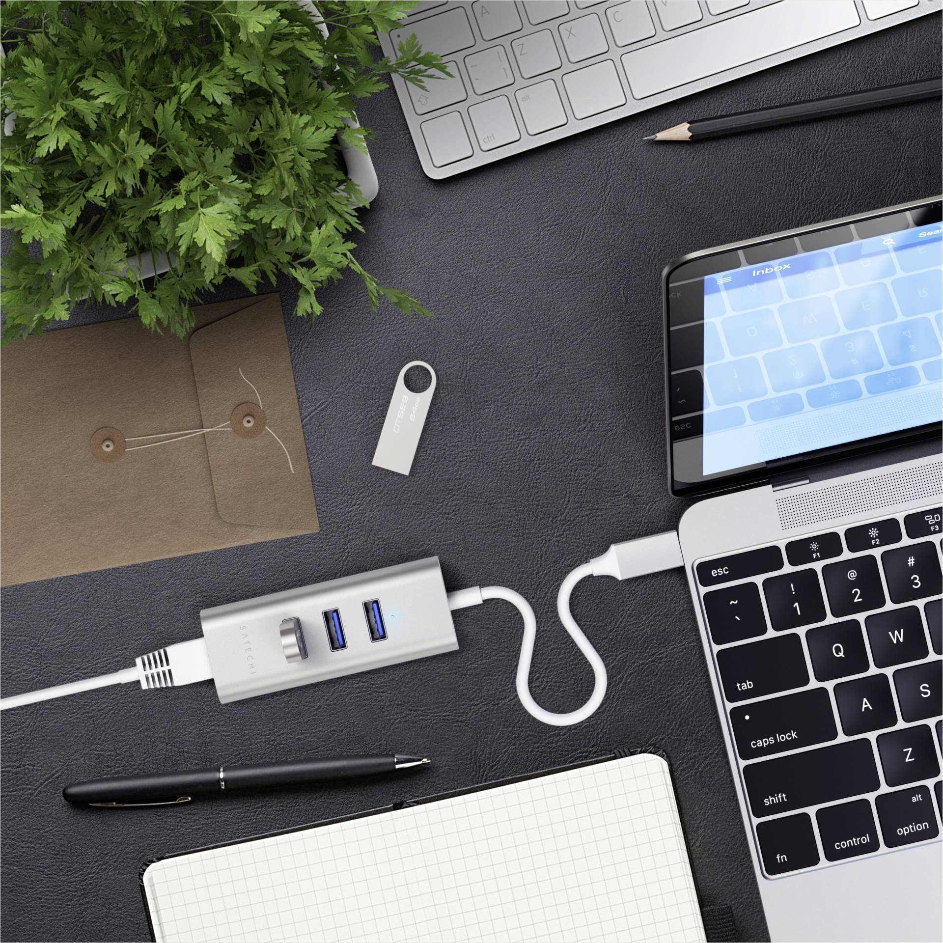Ein Laptop ist über ein USB-Kabel mit einem Multiport-Adapter verbunden. Auf dem Tisch liegen Büroartikel wie Stifte und Umschläge.