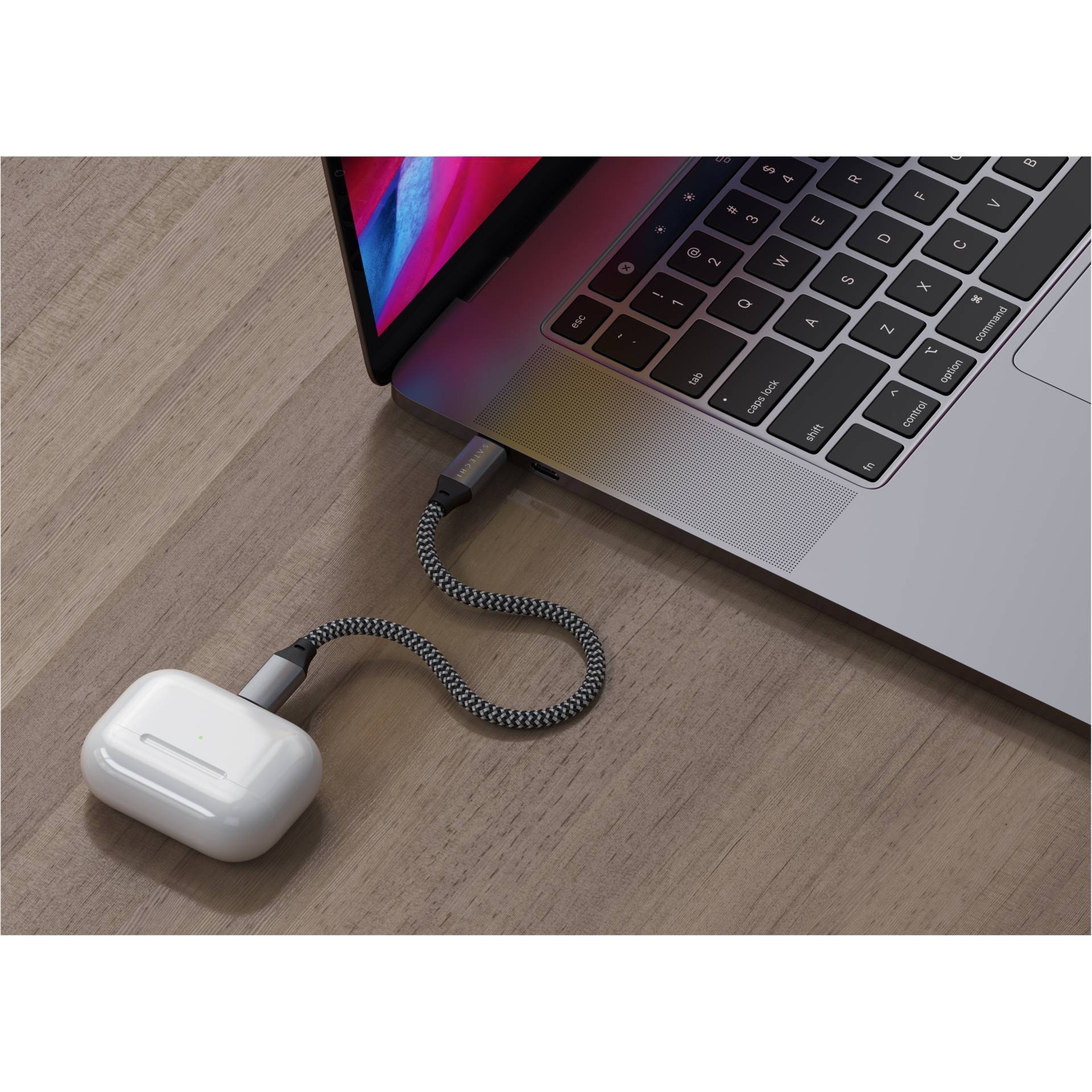 AirPods-Ladekabel ist an einen Laptop angeschlossen und liegt auf einem Holztisch. Der Laptop zeigt einen leuchtenden Bildschirm.