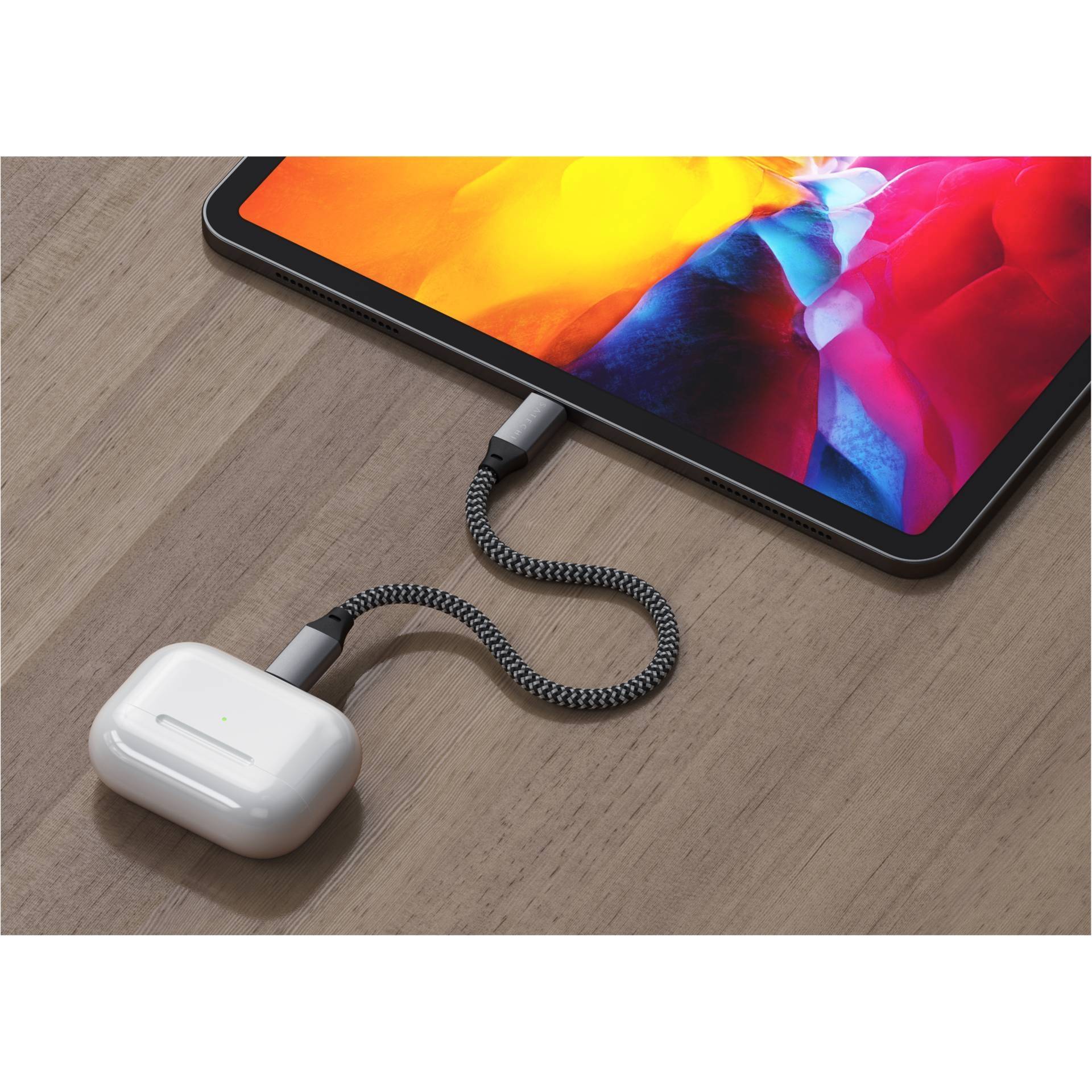 Tablet mit leuchtendem Bildschirm ist mit einem geflochtenen Kabel an kabellose Ohrhörer angeschlossen, auf Holztisch liegend.