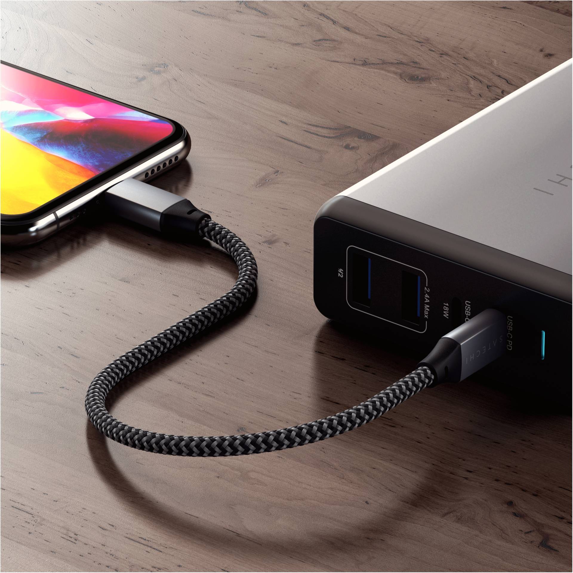 Ein Smartphone ist mit einem geflochtenen Kabel an eine Powerbank angeschlossen, die auf einem Holztisch liegt.