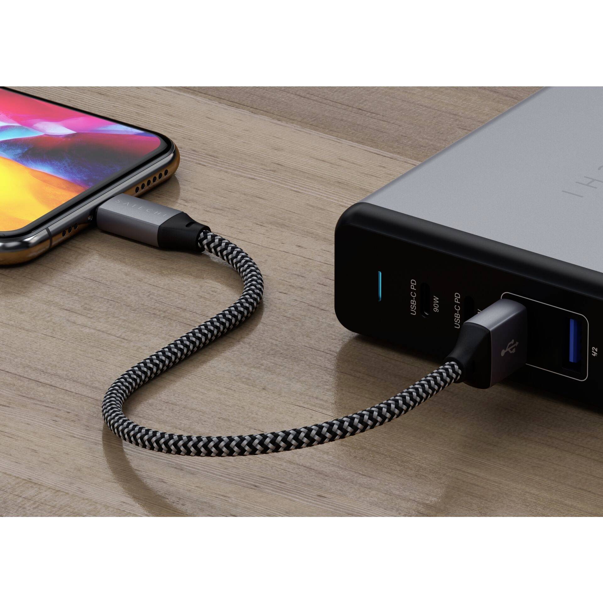 Smartphone mit USB-Kabel an Powerbank angeschlossen; es lädt. Powerbank zeigt Leuchtanzeige. Holztisch im Hintergrund.