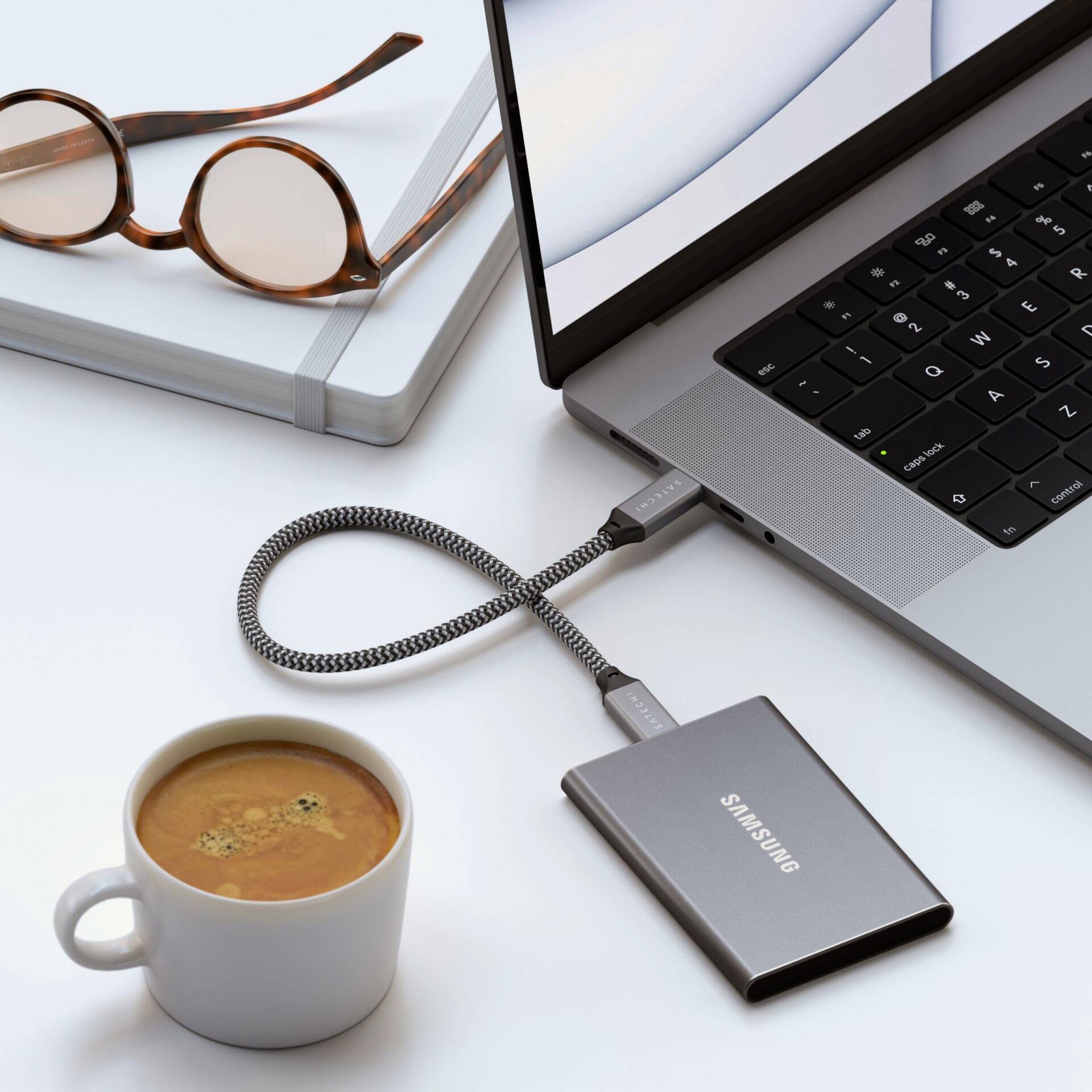 Laptop mit externer Festplatte verbunden, daneben eine Kaffeetasse und eine Brille. Büroarbeitsplatz-Szene mit stilvollem Zubehör.