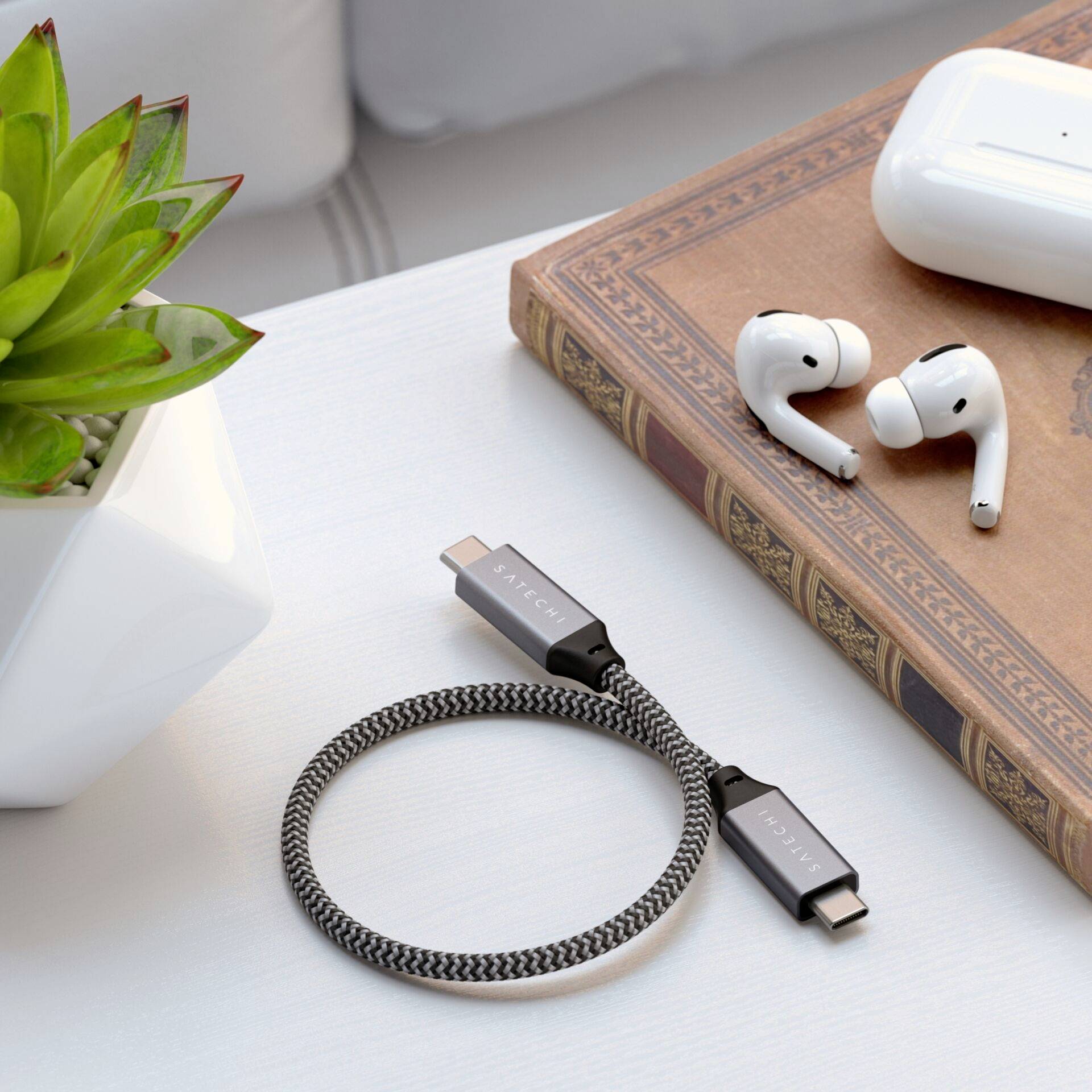 Ein Ladekabel, kabellose Ohrhörer und ein Pflanzenbehälter auf einem Tisch symbolisieren Technologie und Natur im Einklang.