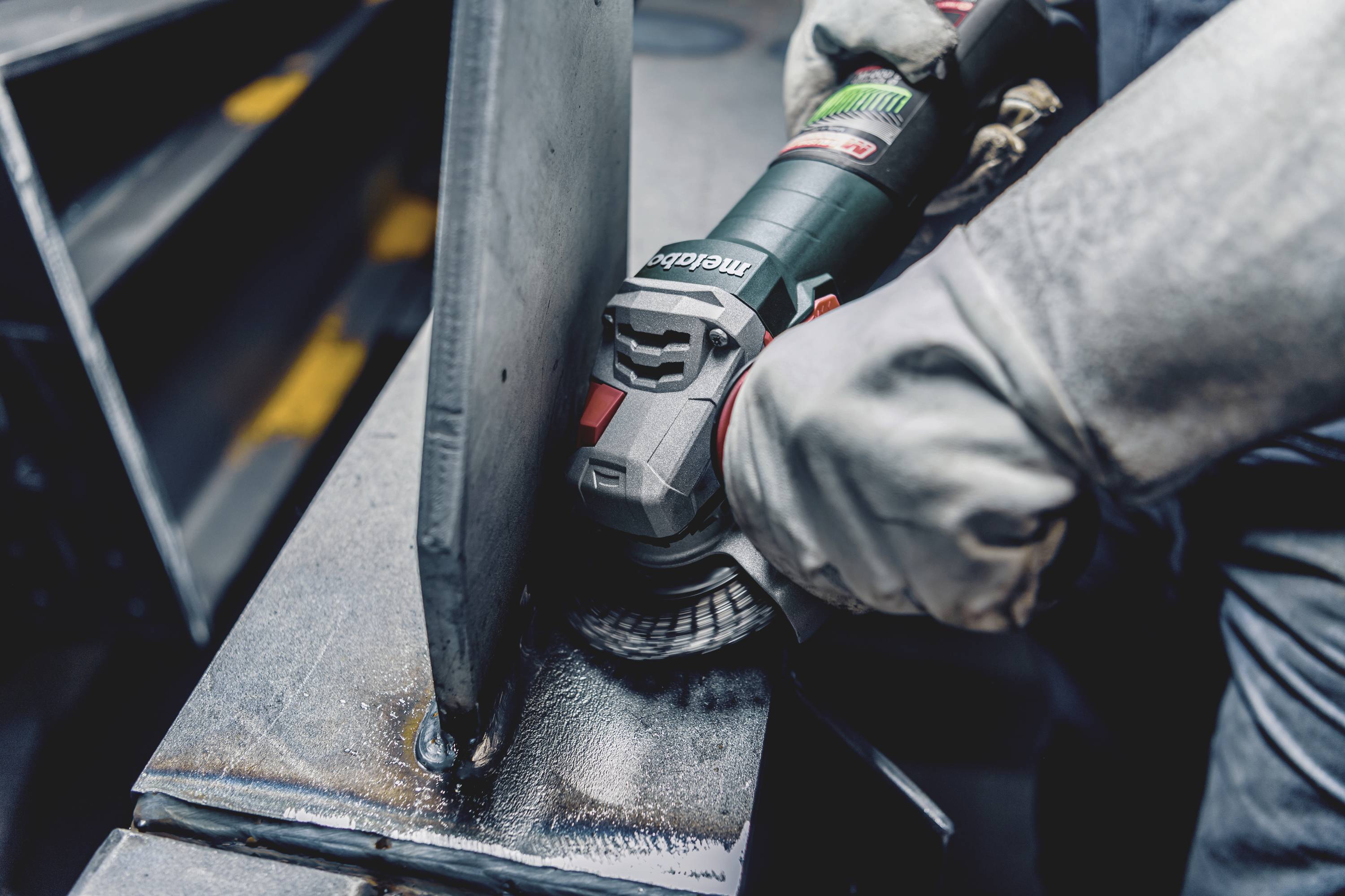 Eine Person schleift mit einem Winkelschleifer Metall. Schutzkleidung und Handschuhe sind sichtbar, was sichere Arbeitsbedingungen zeigt.