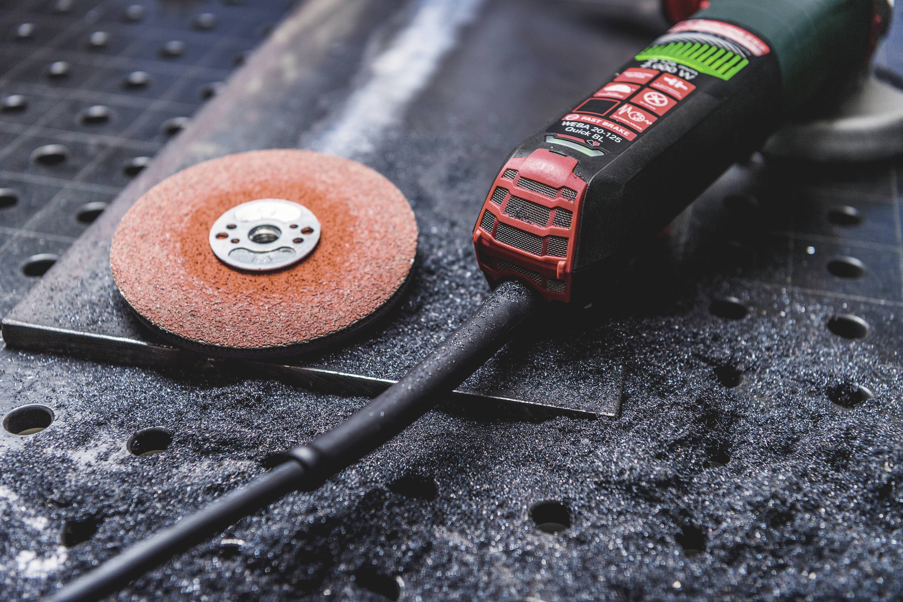 Eine rote Schleifscheibe und ein elektrisches Schleifwerkzeug liegen auf einem staubigen Metalltisch, bereit zur Bearbeitung von Materialien.