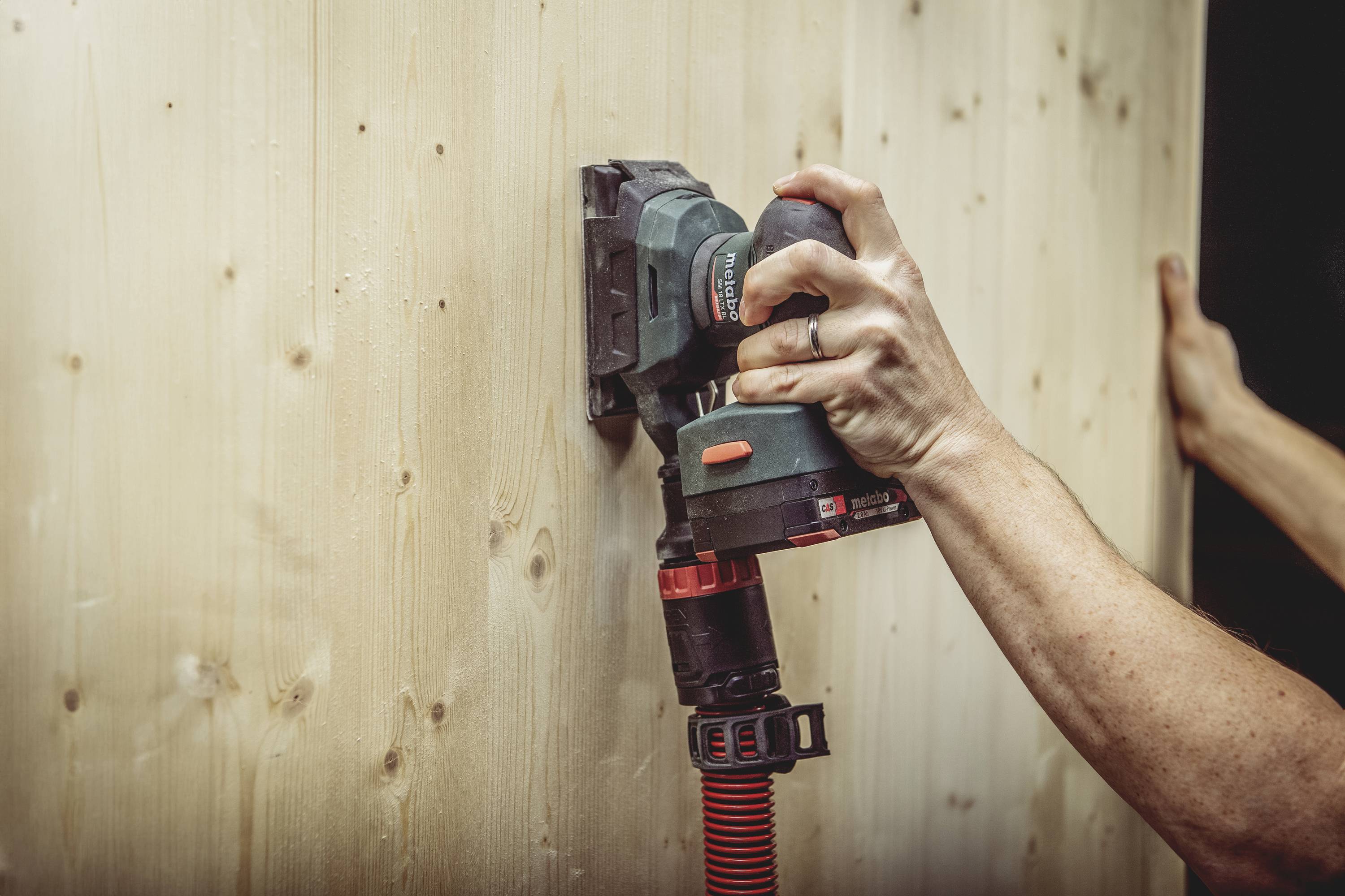 Eine Person schleift mit einem elektrischen Schleifgerät Holz, vermutlich für eine Renovierungs- oder Bauarbeit.