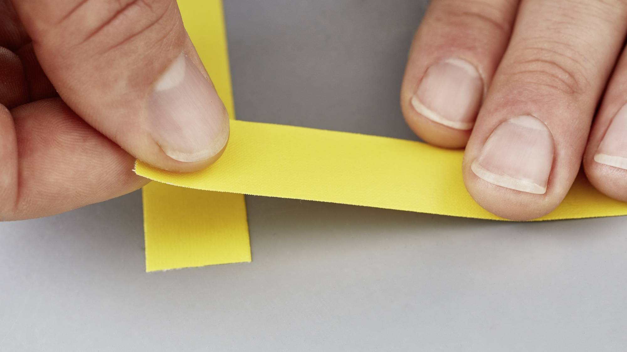 Zwei Hände falten ein gelbes Papierband schräg übereinander, möglicherweise im Rahmen einer Bastelei oder zum Verpacken.