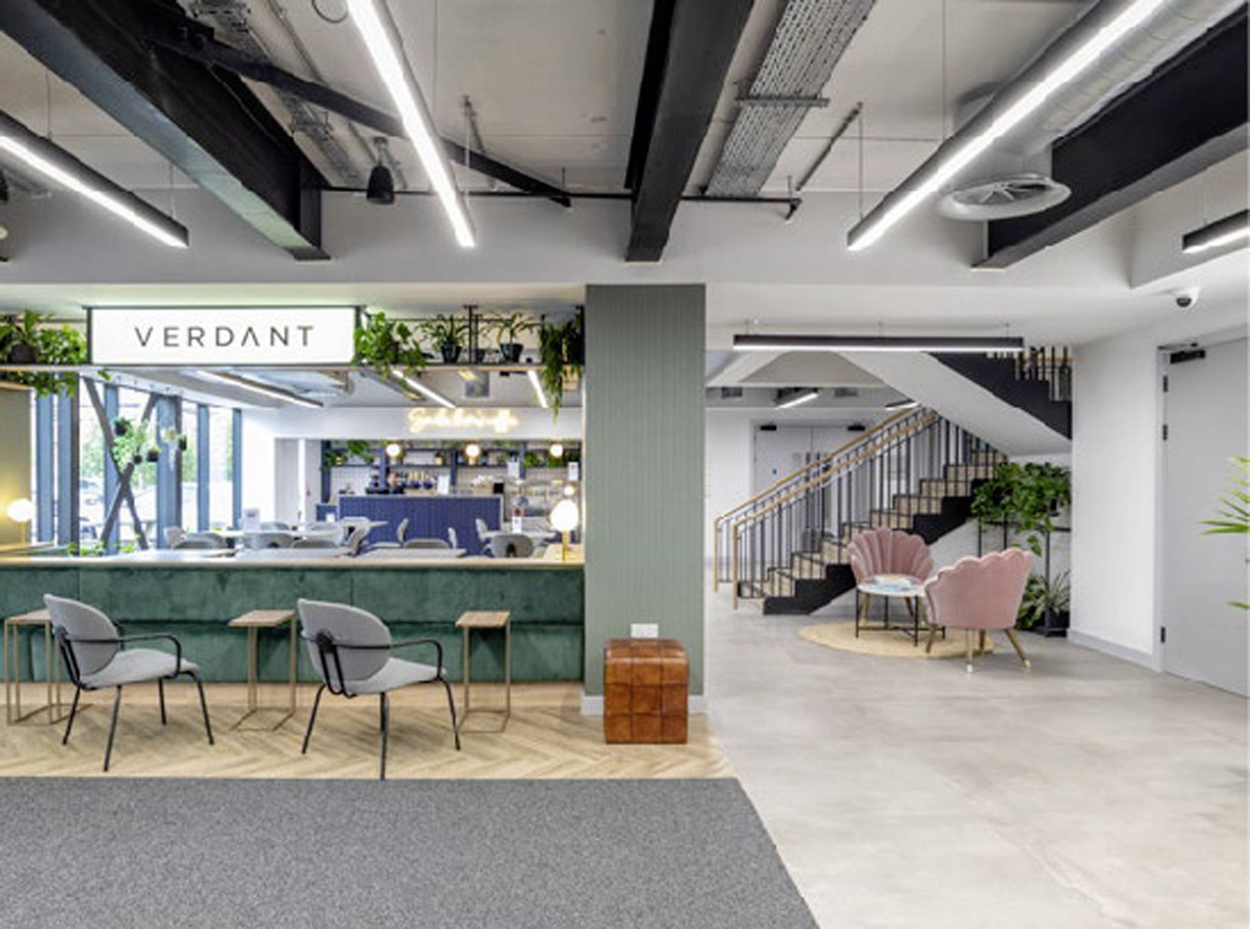 Modernes Büro mit offenen Sitzbereichen, Treppe im Hintergrund. Pflanzen und Beleuchtungselemente schaffen eine einladende Atmosphäre.