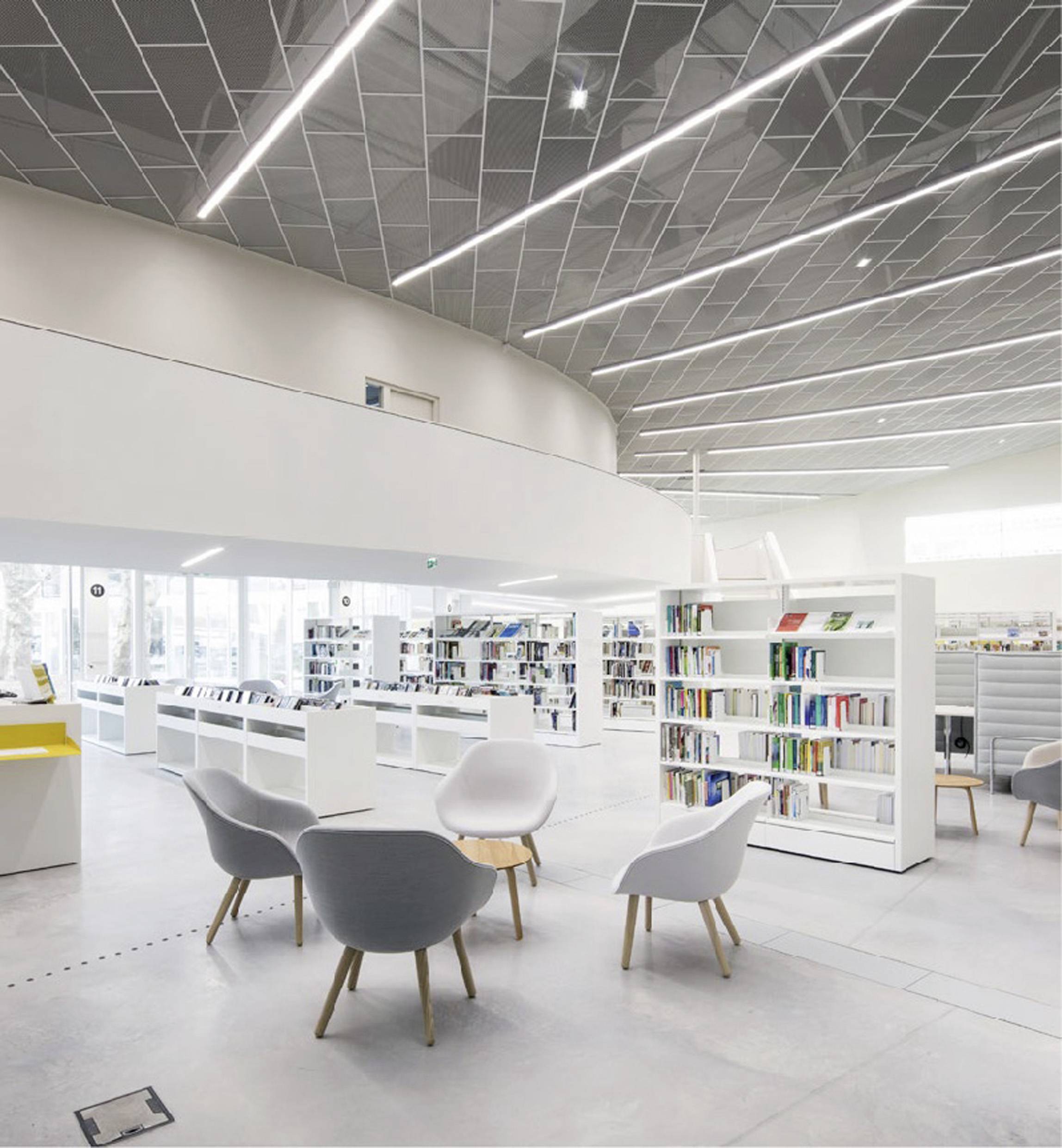Helle, moderne Bibliothek mit weißen Regalen, runden Sitzplätzen und großen Fenstern, die viel natürliches Licht einlassen.