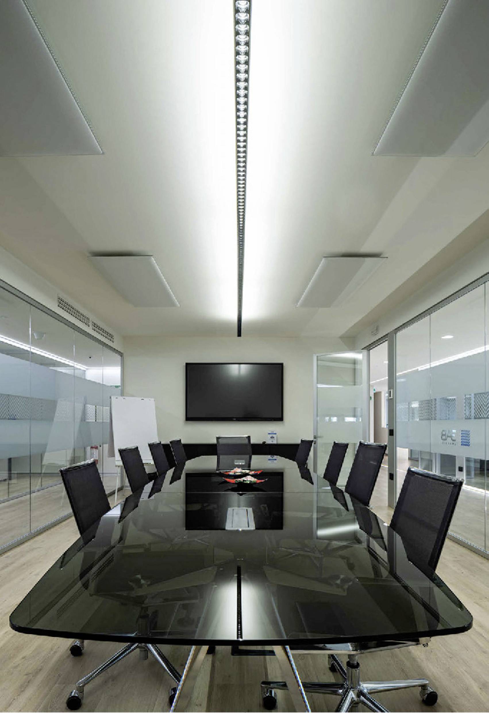 Ein moderner Besprechungsraum mit einem langen, schwarzen Tisch, umgeben von mehreren schwarzen Stühlen. An der Wand hängt ein Flachbildschirm.