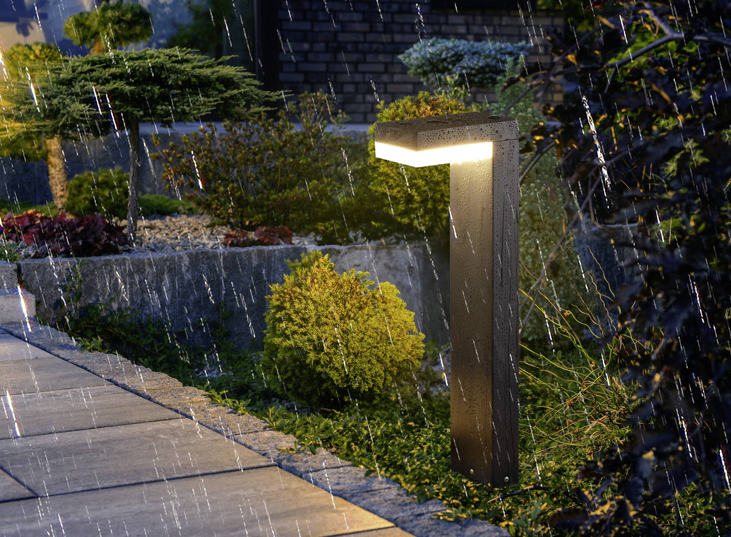 Eine moderne Gartenleuchte erhellt einen regennassen Weg neben gestalteter Bepflanzung und erzeugt eine friedvolle Nachtszene.