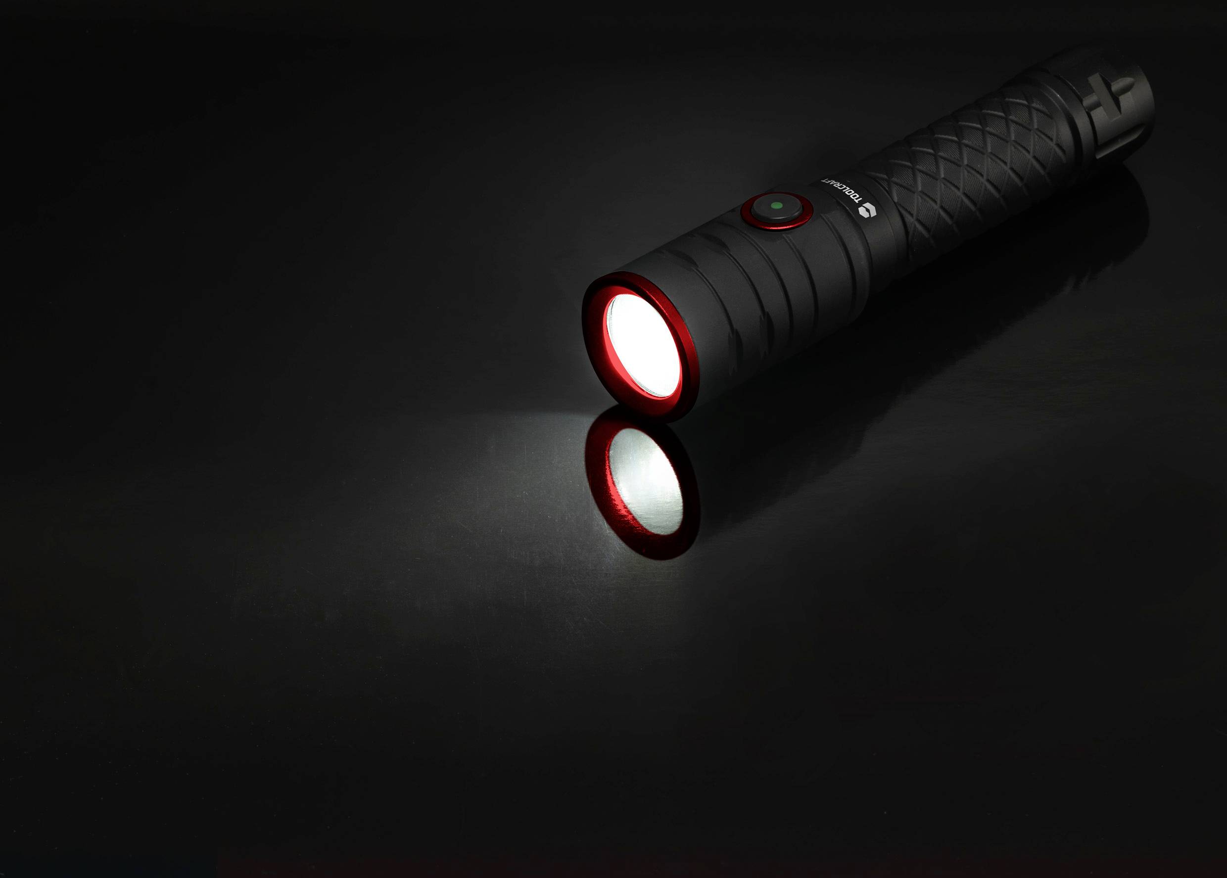 Eine schwarze Taschenlampe, die auf einer glänzenden Oberfläche liegt, leuchtet mit einem weißen Strahl nach vorne.