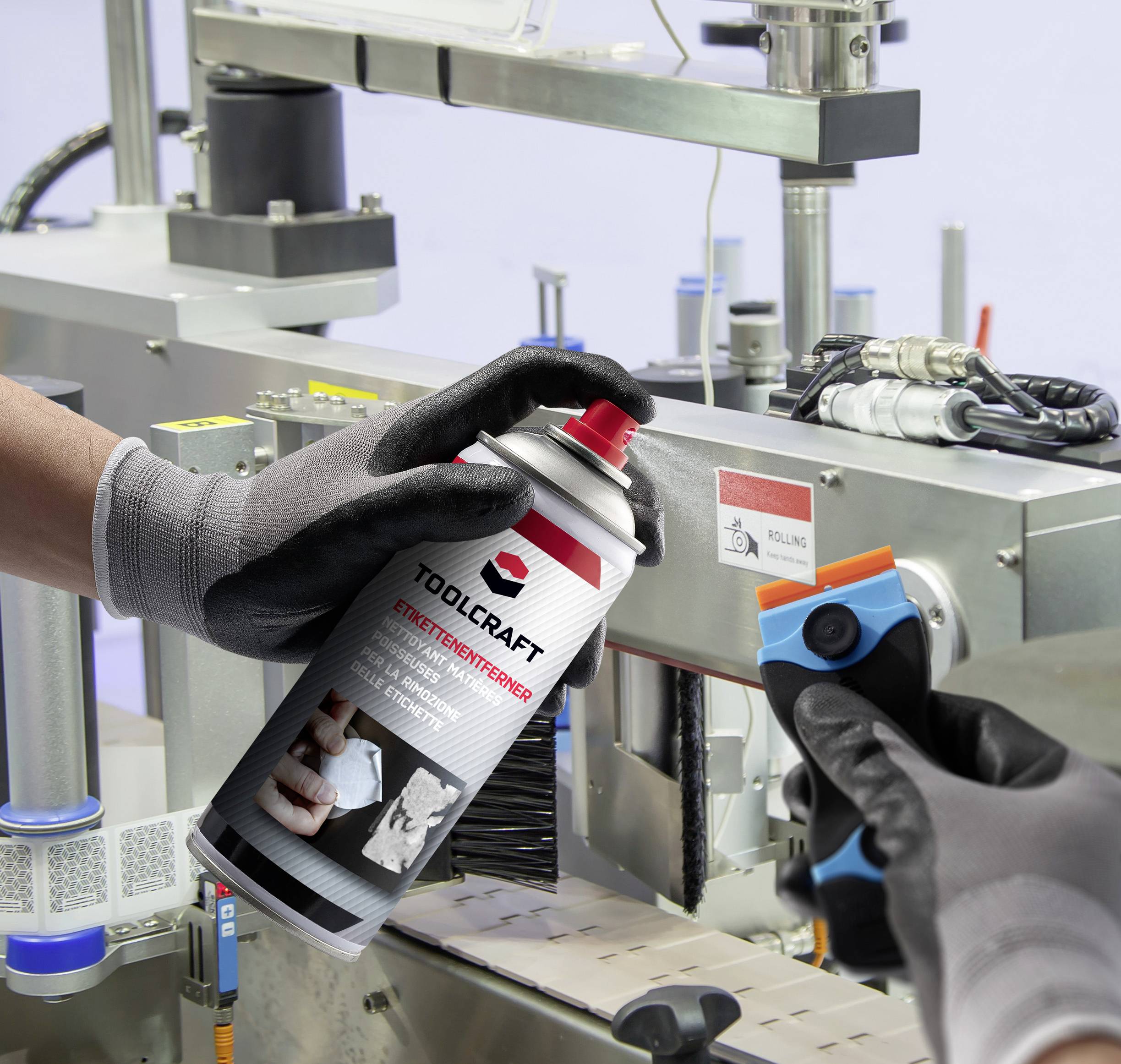 Eine Person mit Handschuhen sprüht Werkzeugschutzspray auf eine Maschine, während sie einen Schaber hält.
