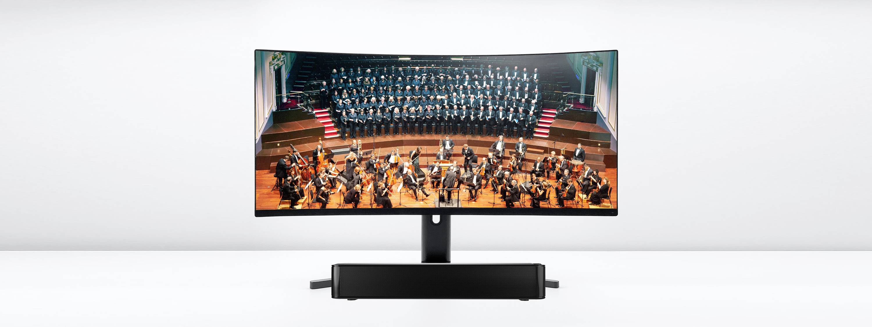 Ein Monitor zeigt eine Aufführung eines Orchesters mit einem Chor im Hintergrund auf einer Bühne, LED-Leuchten im Vordergrund.
